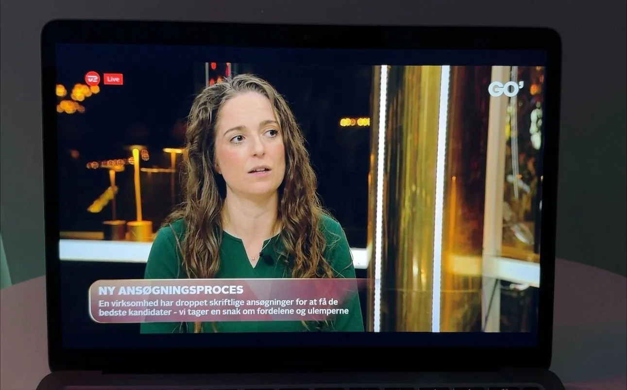 En tv-skærm viser en kvinde med brunt, krøllet hår, der taler i en nyhedsudsendelse om en virksomhed, der har modtaget skriftlige ansøgninger.