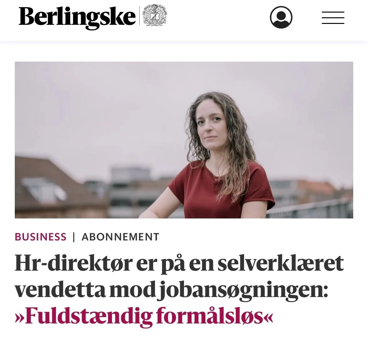 En kvinde med brunt hår og rødt t-shirt står på en tagterrasse med bygningskroppe i baggrunden.