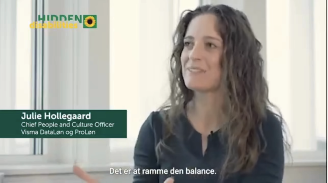 Julie Hollegaard sidder i et kontorlokale, taler og smiler, med tekst der viser hendes navn og titel.