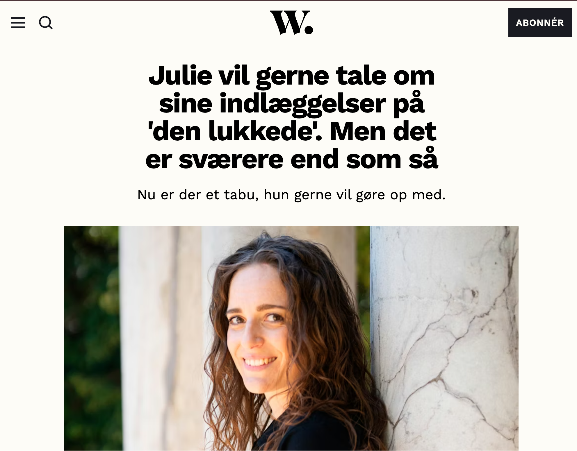 En ung kvinde med brunt, krøllet hår smiler og kigger mod kameraet. Bag hende er en væg af marmor og nogle grønne træer.