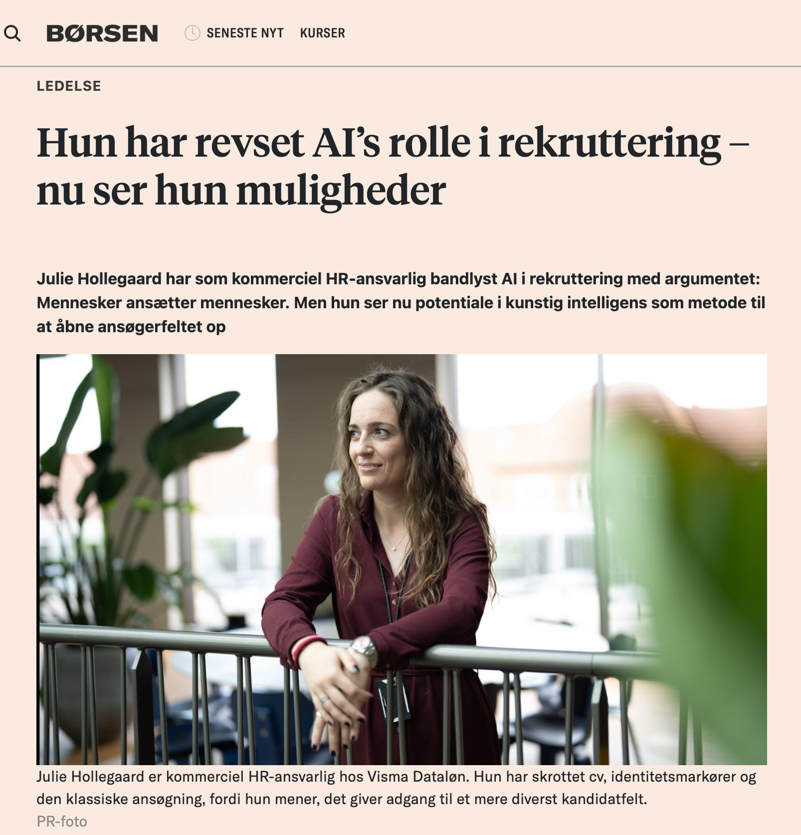 Julie Hollegaard sidder i en kontorbygning med store vinduer, omgivet af grønne planter, og smiler.