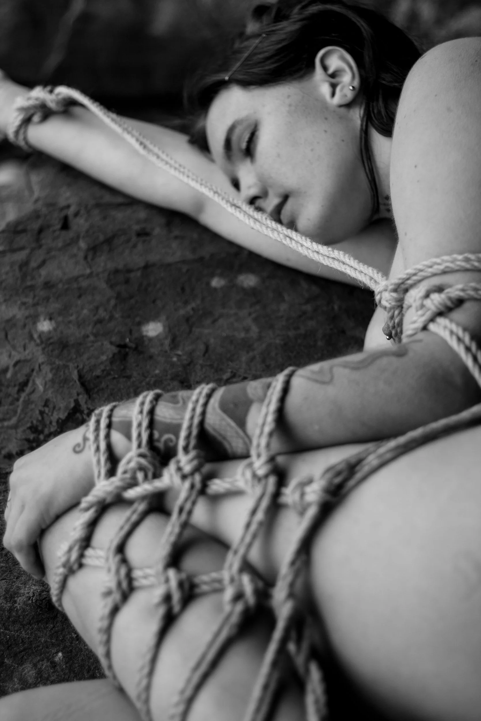 woman on big rock, cradled position, with rope on her. washed up mermaid shibari shoot in uk
