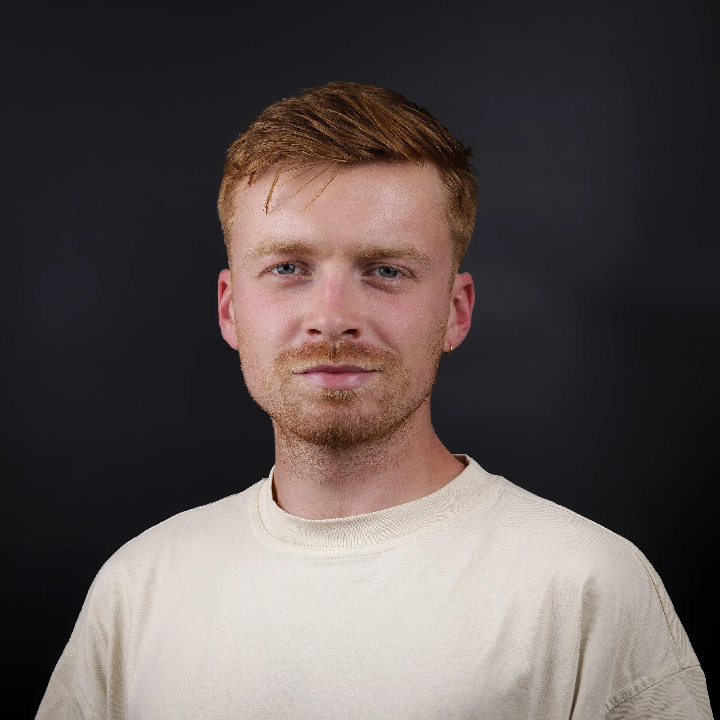 Close-up of a young man with red hair, blue eyes, wearing a white shirt, against a black background.