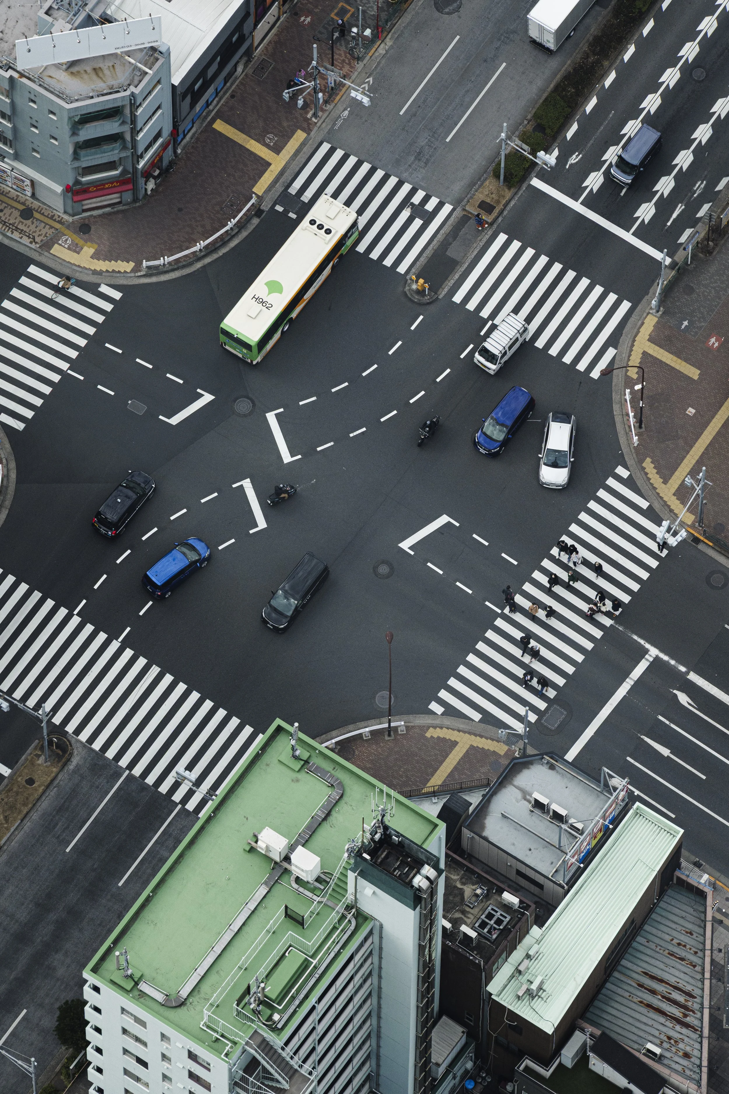 An aerial view of city streets showing a bus, cars, motorcycles, crosswalks, sidewalks, buildings, and streetlights.