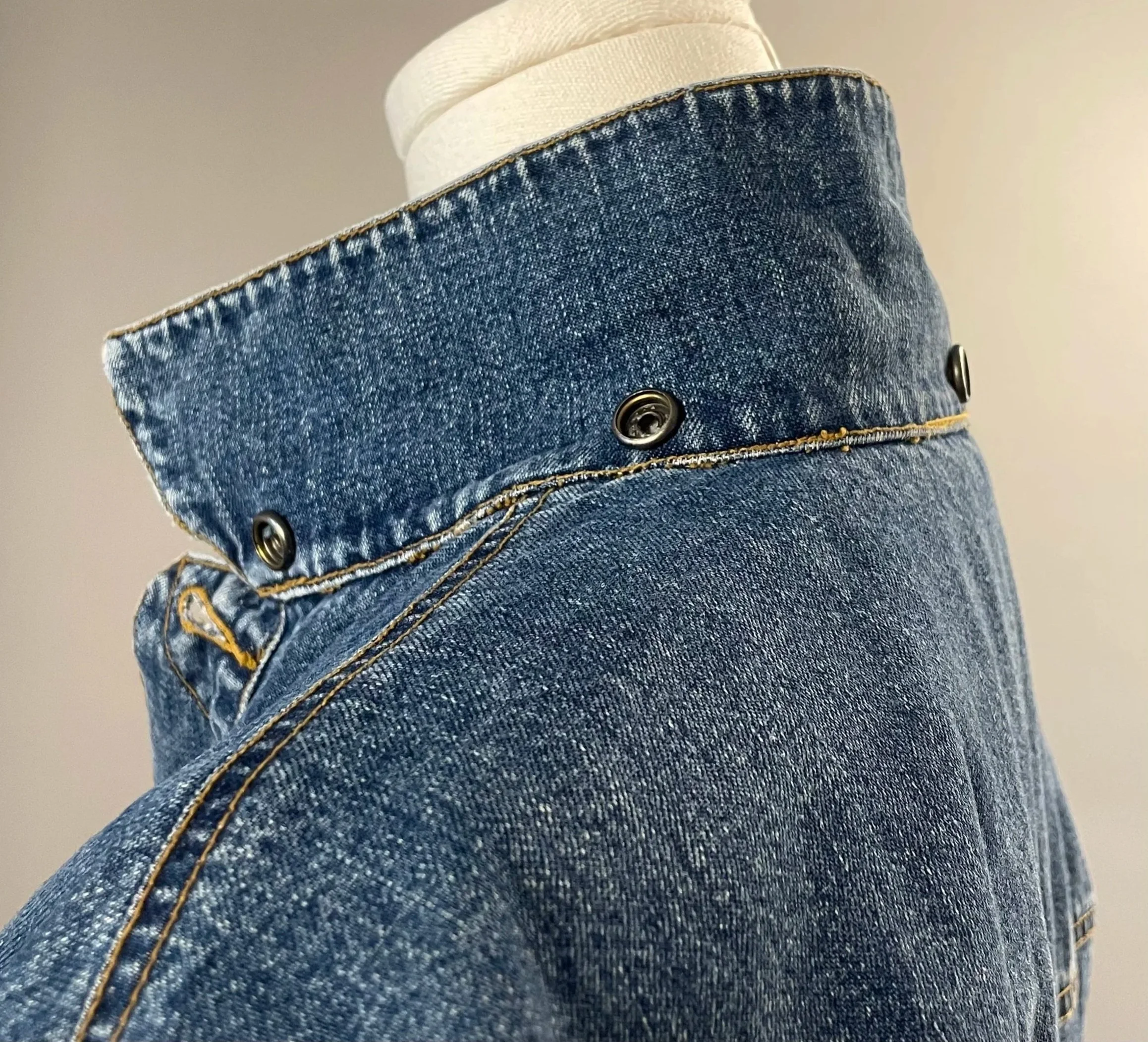 Detailed texture shot of a medium-wash blue cotton denim jacket collar, showcasing a DKNY sample jacket on a white garment form.