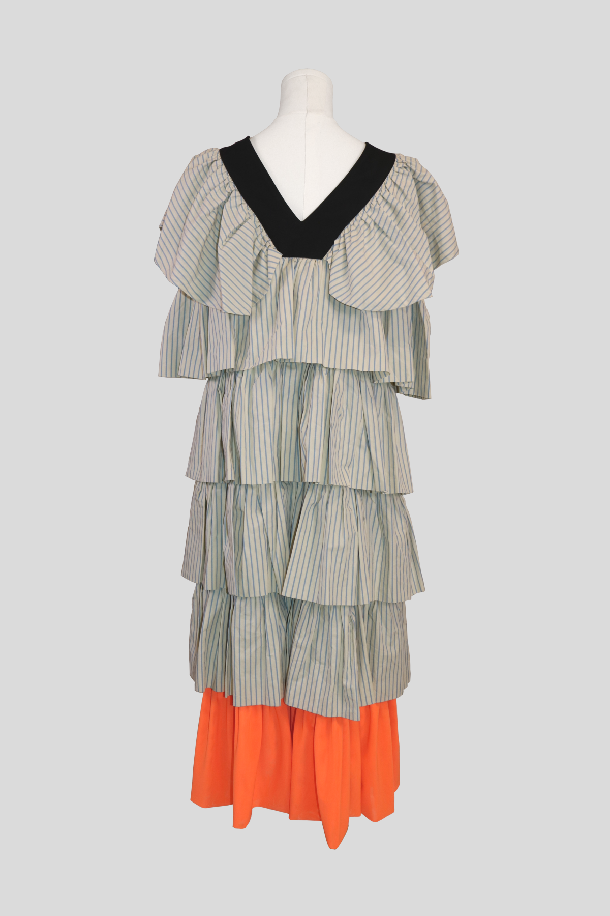 full back view of the joanne hynes dress. showcases the continuous tiers of structured blue and white pinstriped frills flowing vertically, balanced by the vibrant orange pleated panel along the bottom hemline.