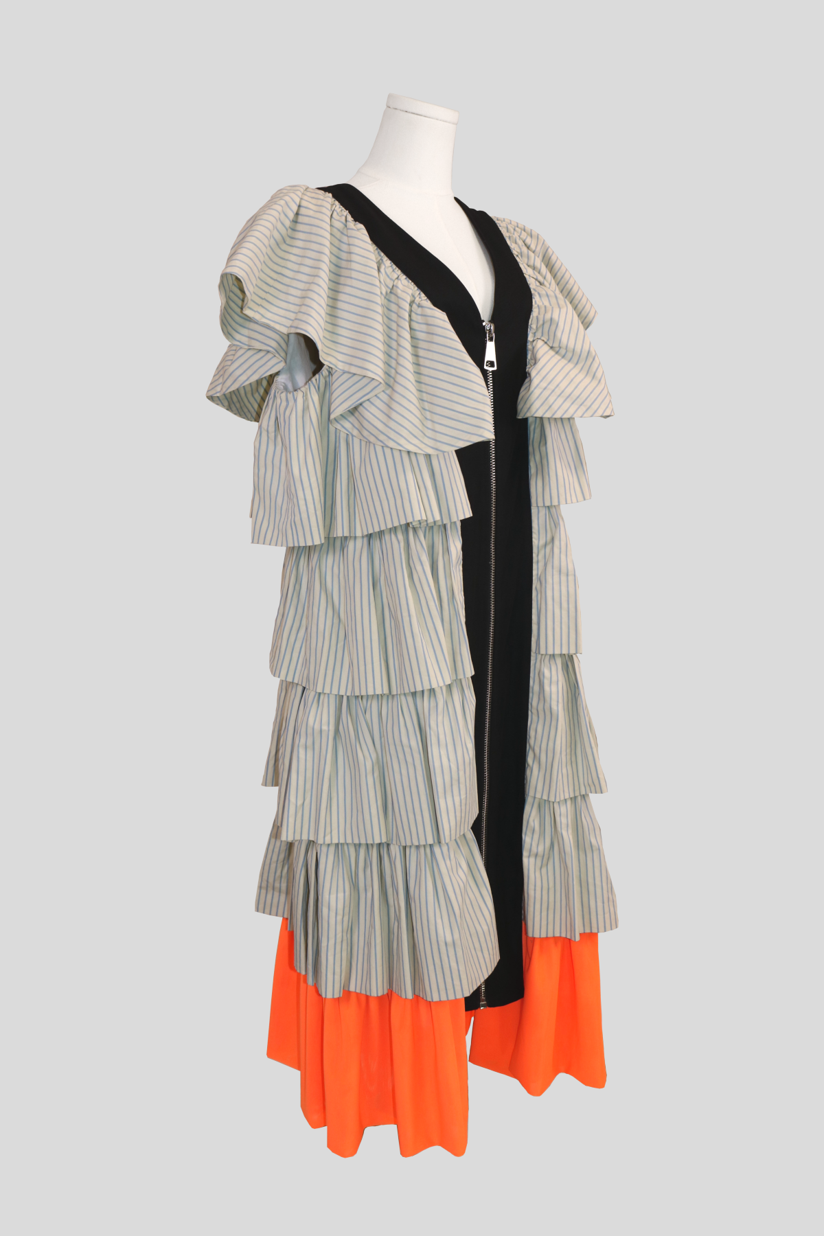 profile view of the joanne hynes pinstripe frill dress. highlights the sculptural dimension and high volume of the tiered ruffles extending outward from the armholes down to the contrasting orange lower trim.