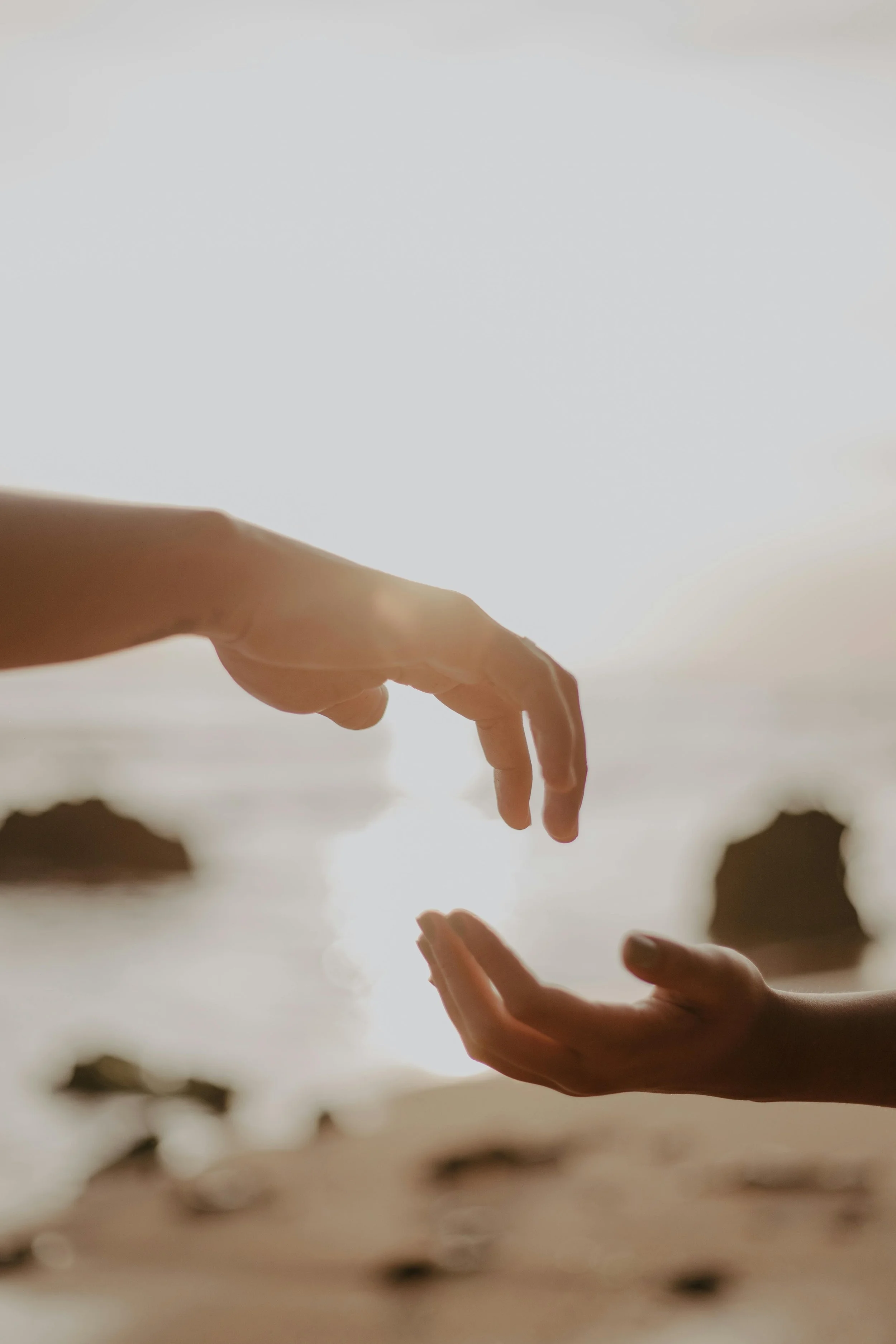 A couple reaches out their hands to one another on the San Jose beach after an energy healing session with Flourish & Flow.