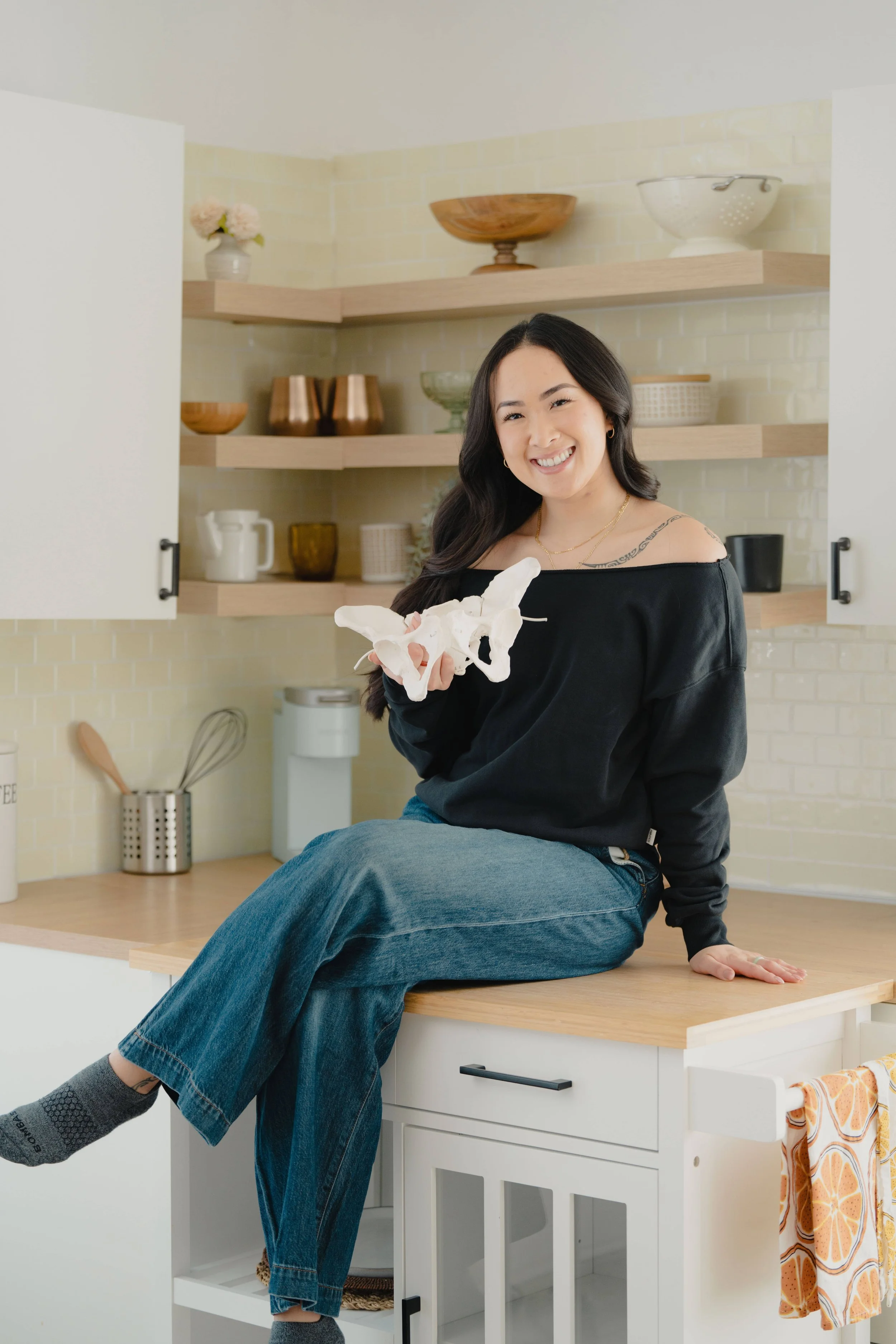 Holding a pelvis model, birth doula Jamee Leann Vasquez sits on a counter in Santa Clara.