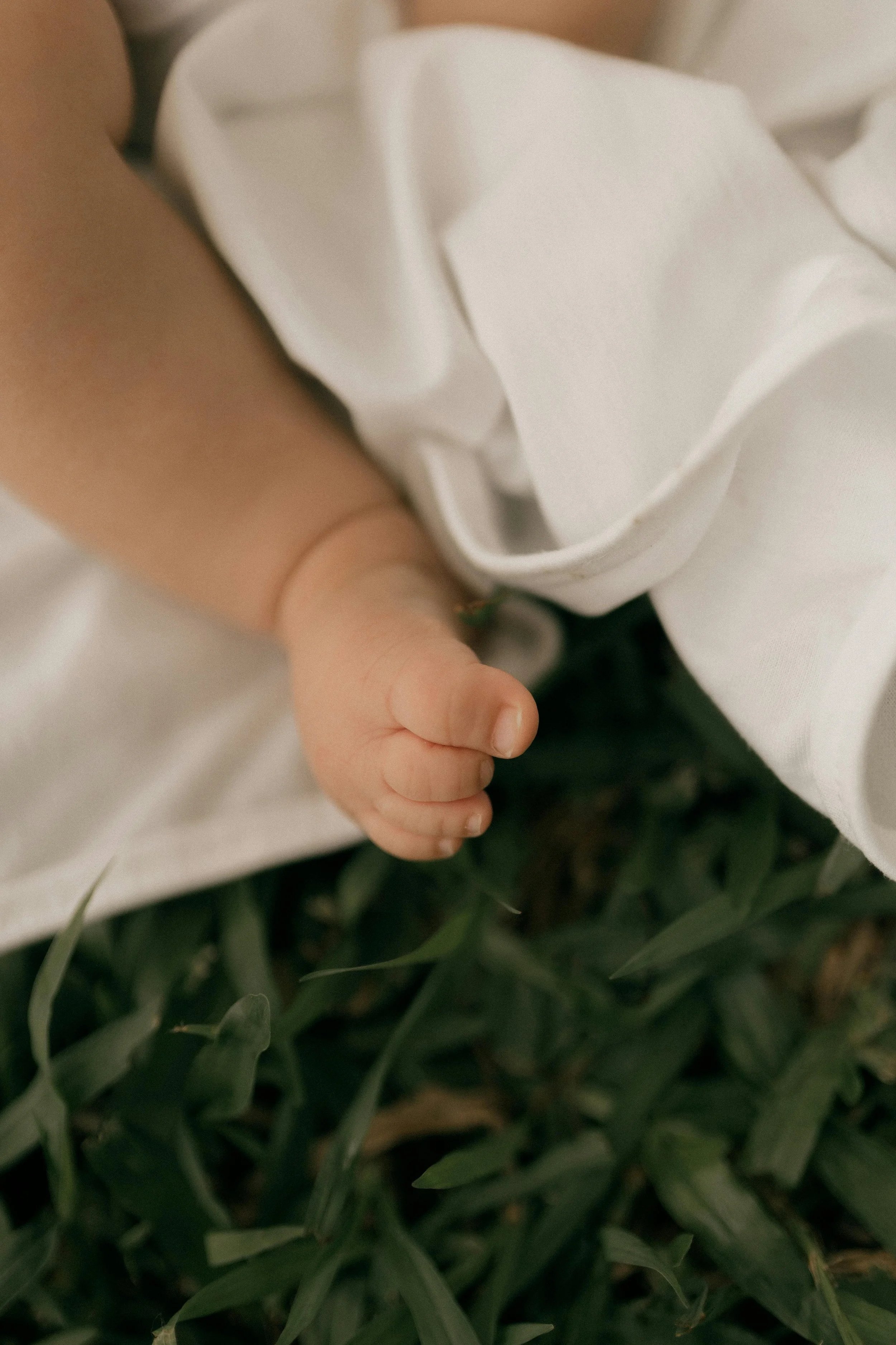A newborn, whose parents are getting daytime postpartum support from Flourish & Flow, rests their legs on a white blanket outside in Santa Clara, California.