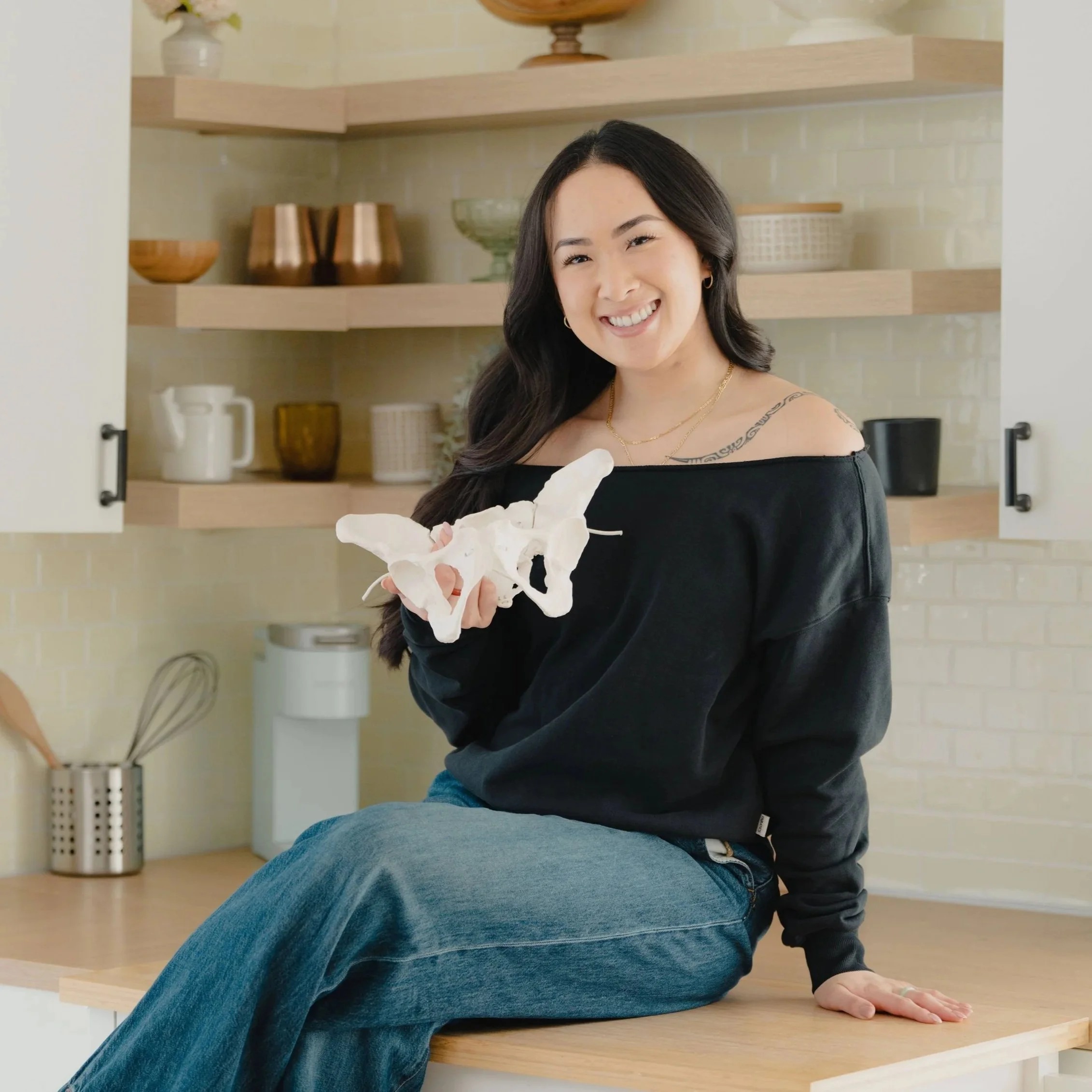 Birth doula Jamee Leann Vasquez  holds a model of a pelvis while sitting on the counter in her California home.