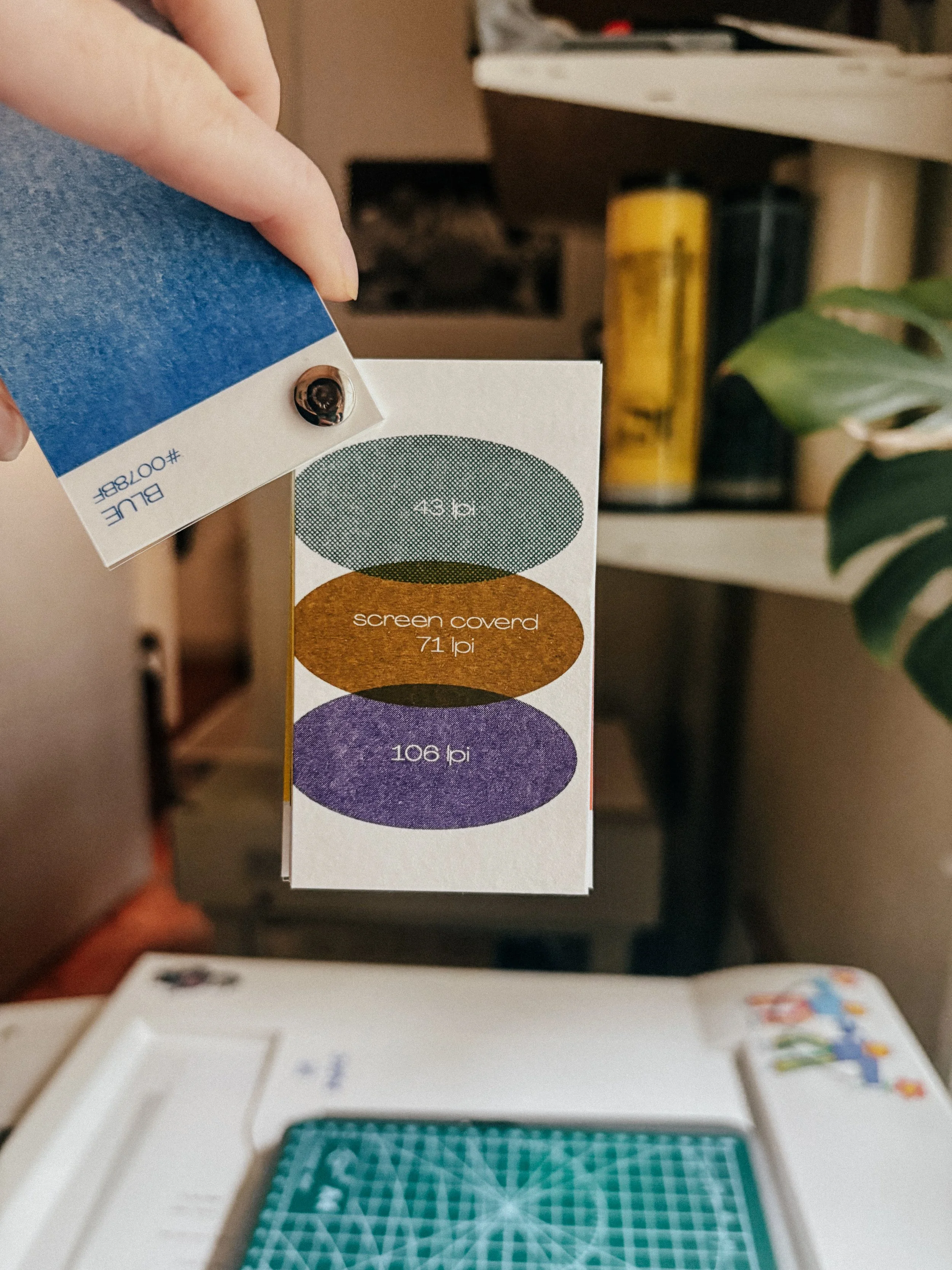 Close-up of a person's hand pinning a circular button onto a paper, with a board game below and snacks on a table in the background.