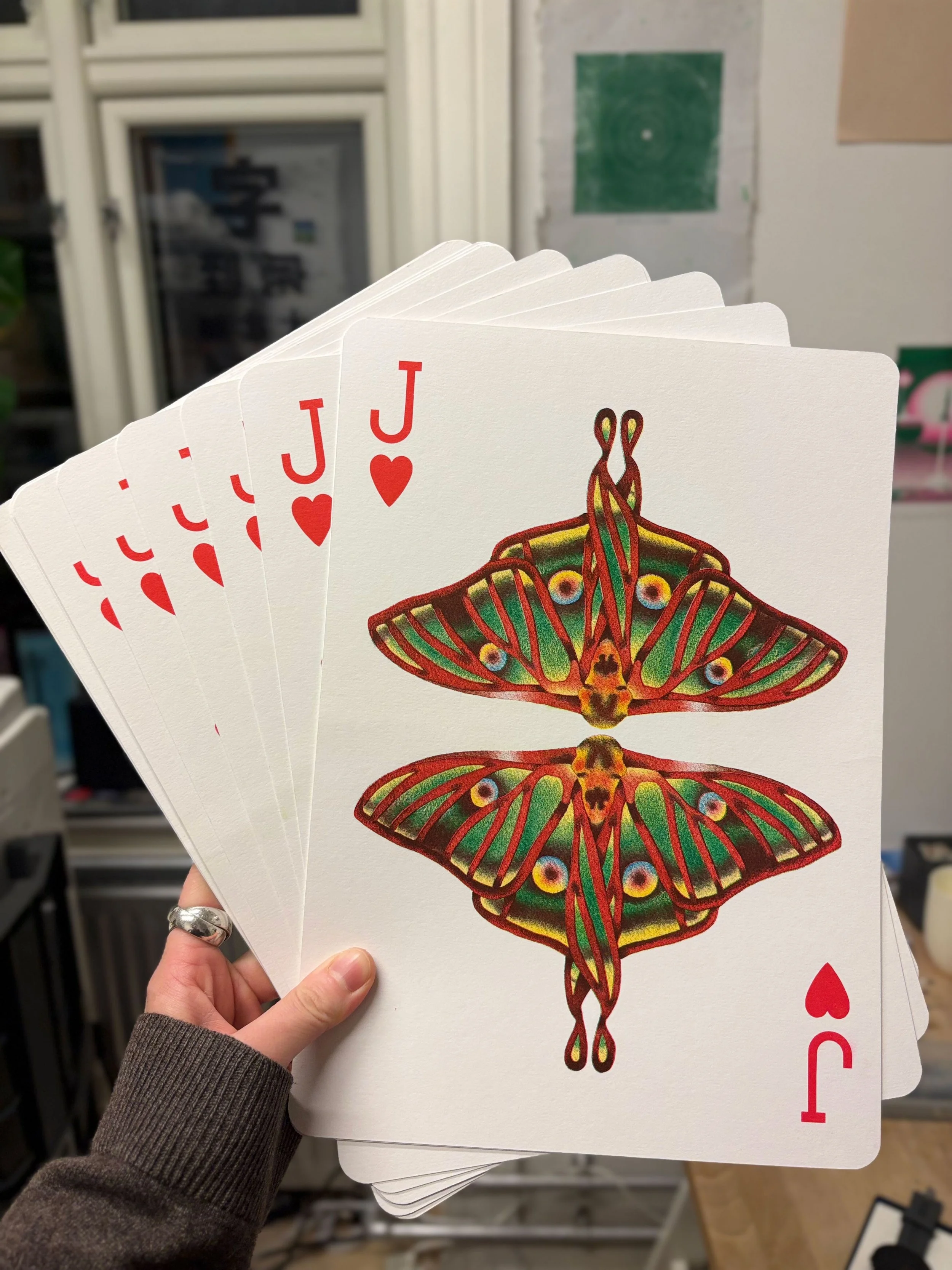 Hand holding playing cards featuring a colorful butterfly design, with the ace of hearts card partially visible behind the others.
