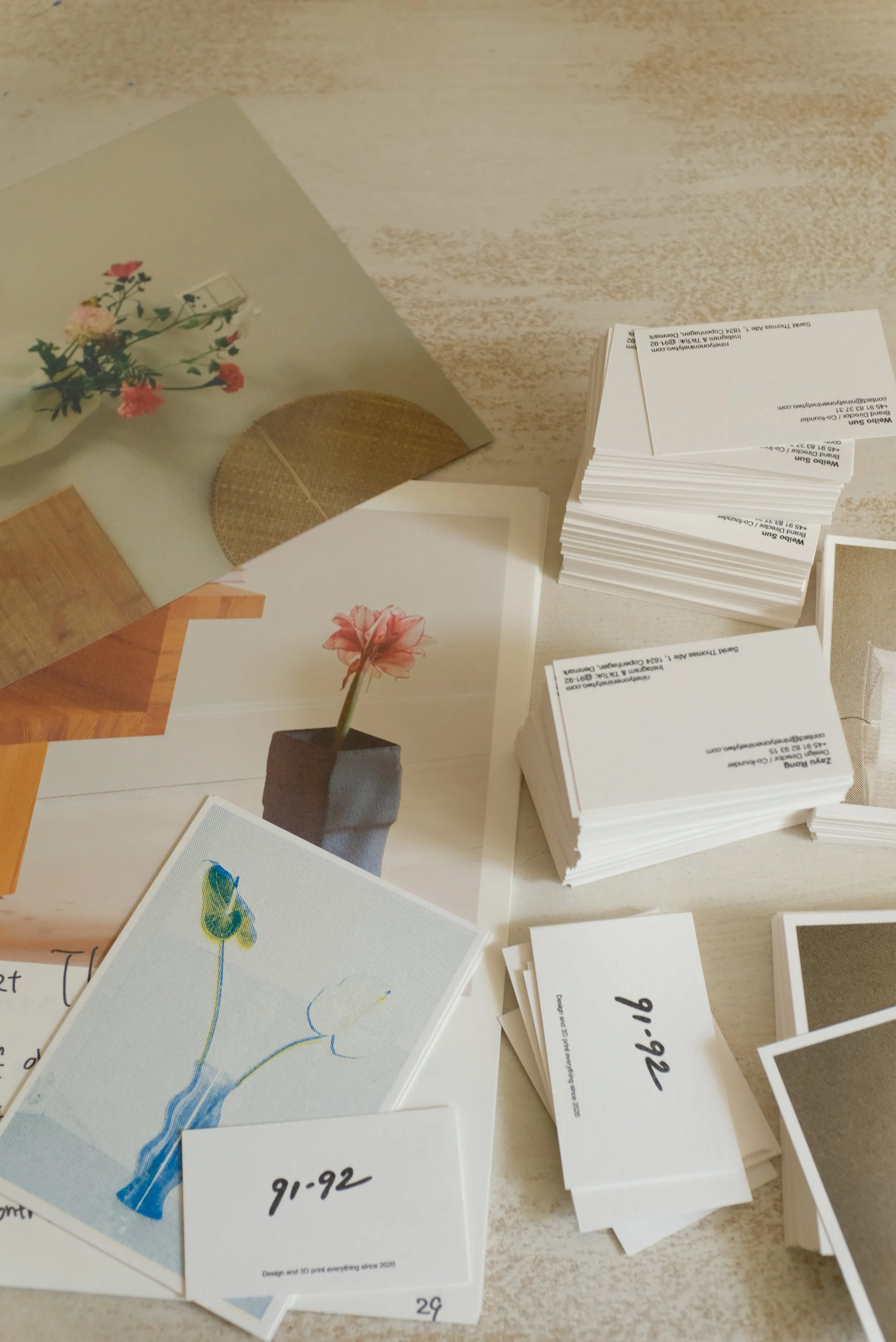 A workspace with printed index cards, some showing photos of flowers and artwork, and some with handwritten numbers or dates. There are sheets and a photo of a flower in a pot.