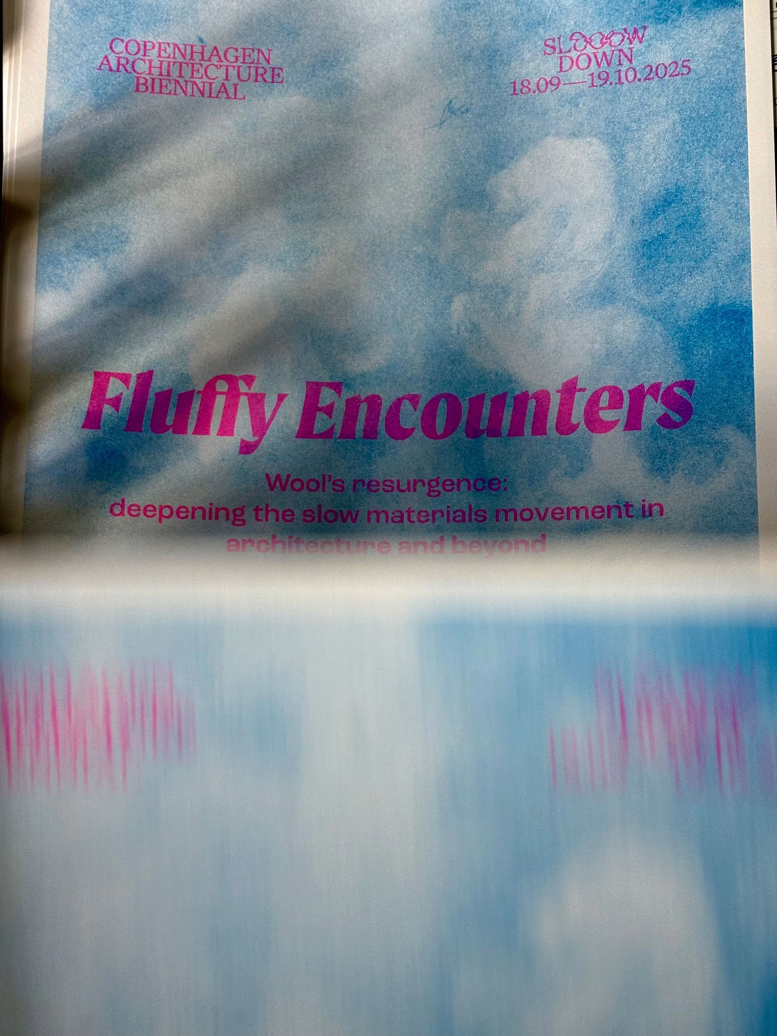 Flyer with a blue sky background and partly cloudy clouds. Pink text reads: "Copenhagen Architecture Biennial" and "Slow Down 18.09—19.10.2025." The title "Fluffy Encounters" appears in large pink letters, with additional text about wool's resurgence and deepening the slow materials movement in architecture and beyond.