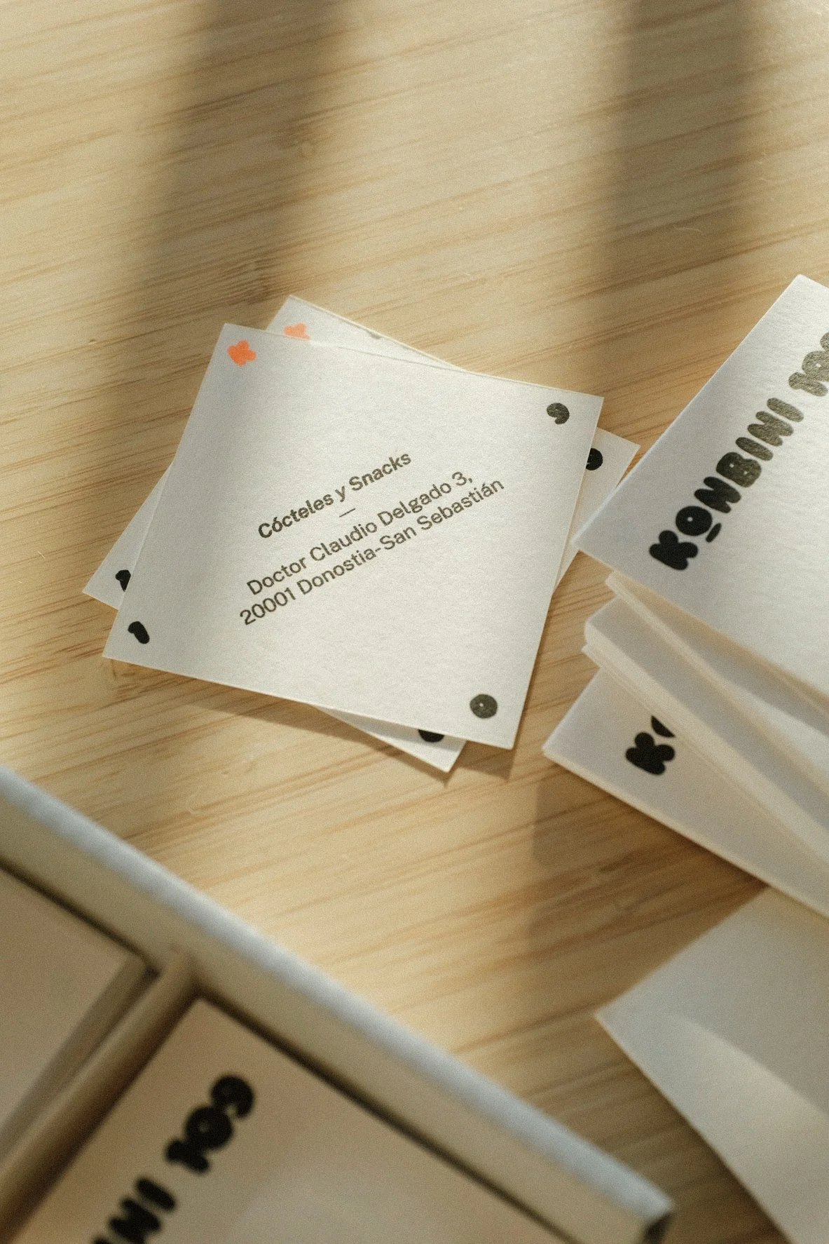 Stack of playing cards on a wooden surface with a note labeled 'Cócteles y Snacks' from Doctor Claudio Delgado, located at 2001 Donostia-San Sebastián.