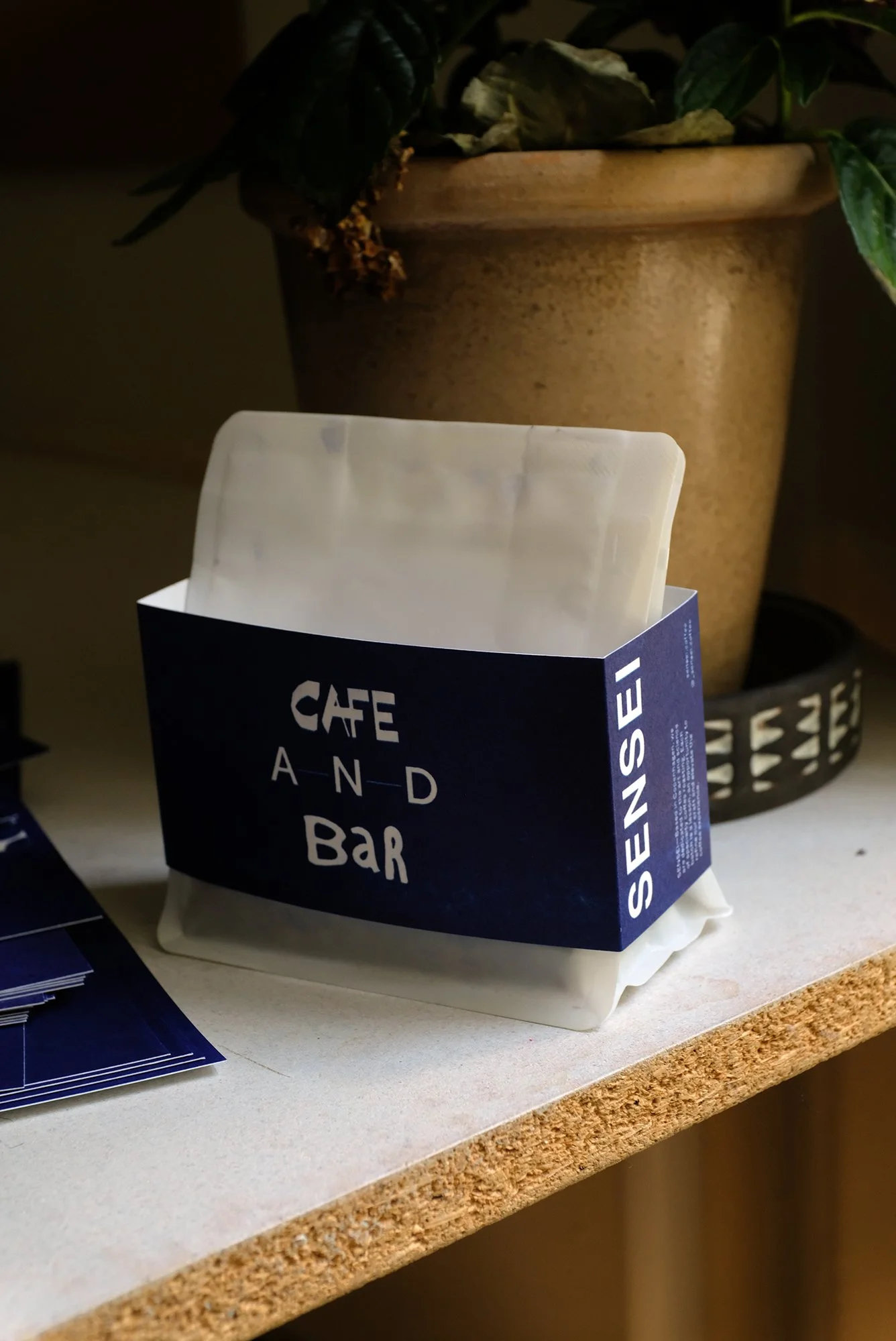 Close-up of a white energy bar in a blue wrapper labeled 'SEVEN SEVEN CAFE AND BAR' on a light-colored countertop next to a potted plant with green leaves.