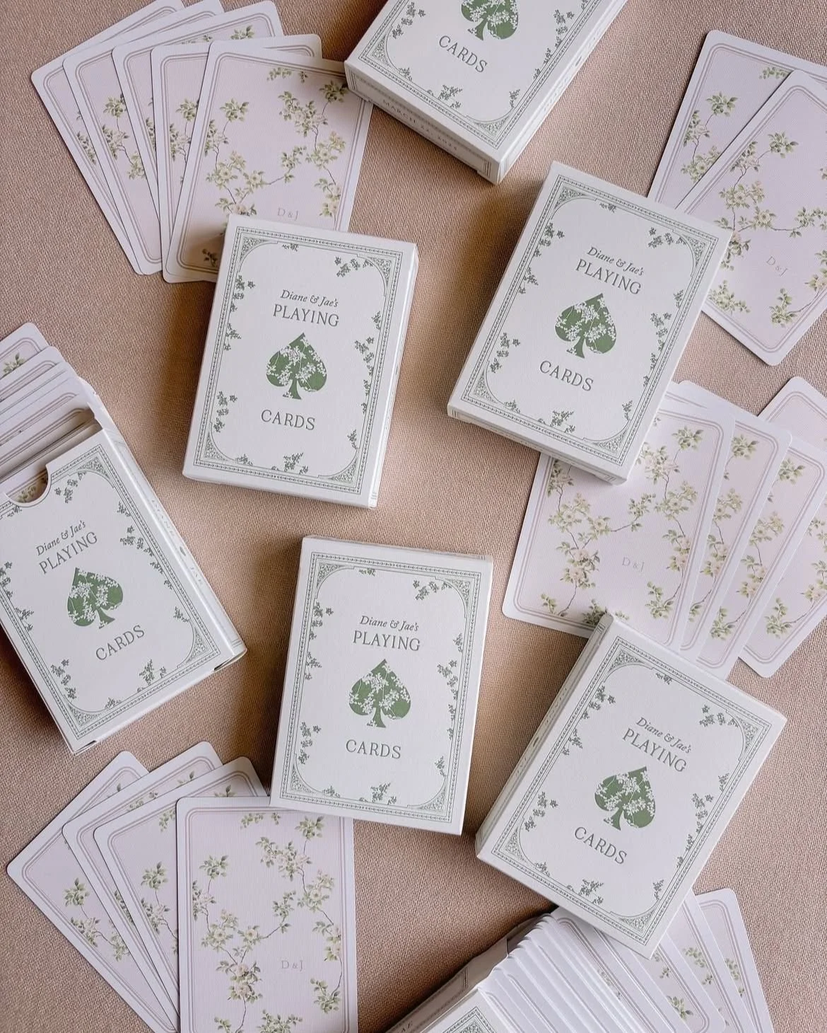 A collection of playing cards and card boxes on a pinkish surface, with some cards face down and others face up showing floral designs.