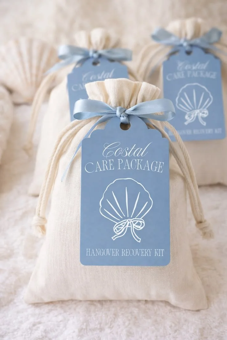 A white drawstring bag labeled "Coastal Care Package" with a seashell illustration and "Hangover Recovery Kit" text, tied with a light blue ribbon.