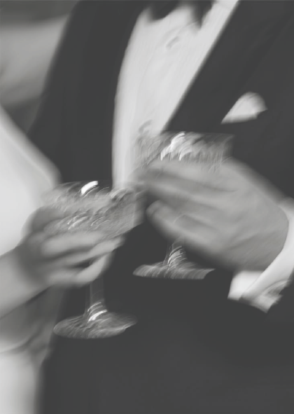 A person in a tuxedo holding a cocktail glass at a formal event.