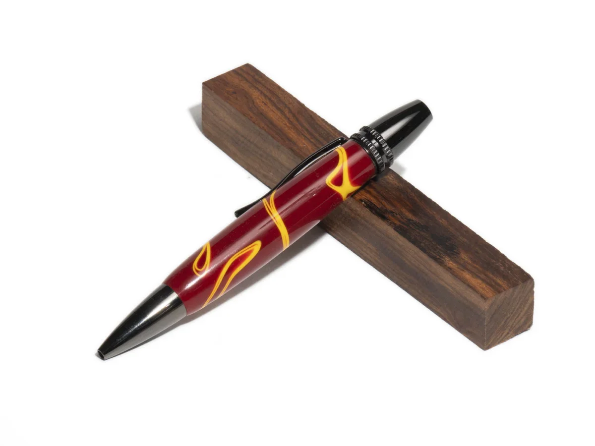 Design‑Kugelschreiber in Rot und Schwarz mit Metallkomponenten, liegend auf einem Holzblock vor hellem Hintergrund