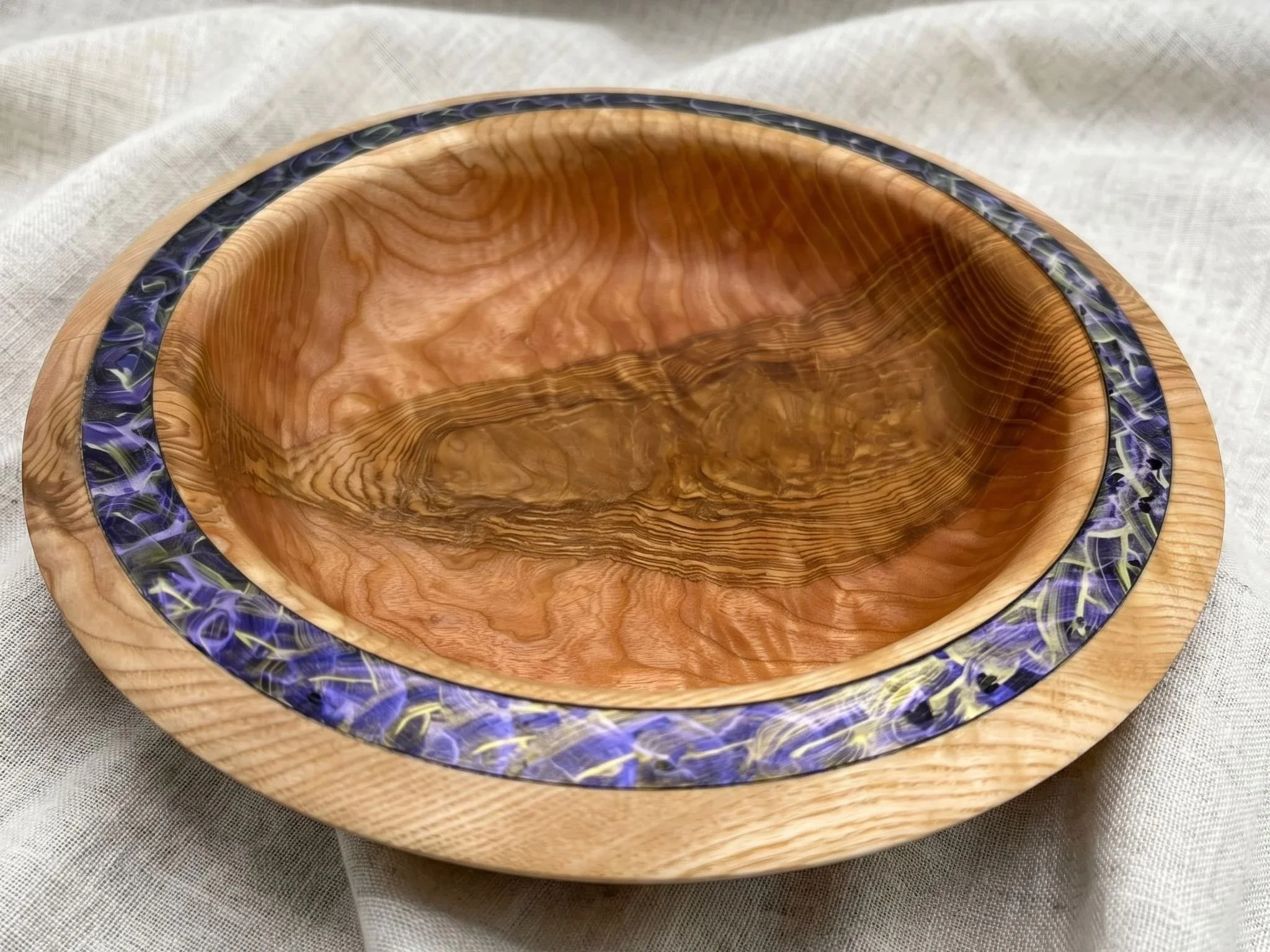 Runde Holzschale mit natürlicher Maserung und dekorativer Einlage am Rand, Innenansicht auf strukturierte Holzoberfläche.