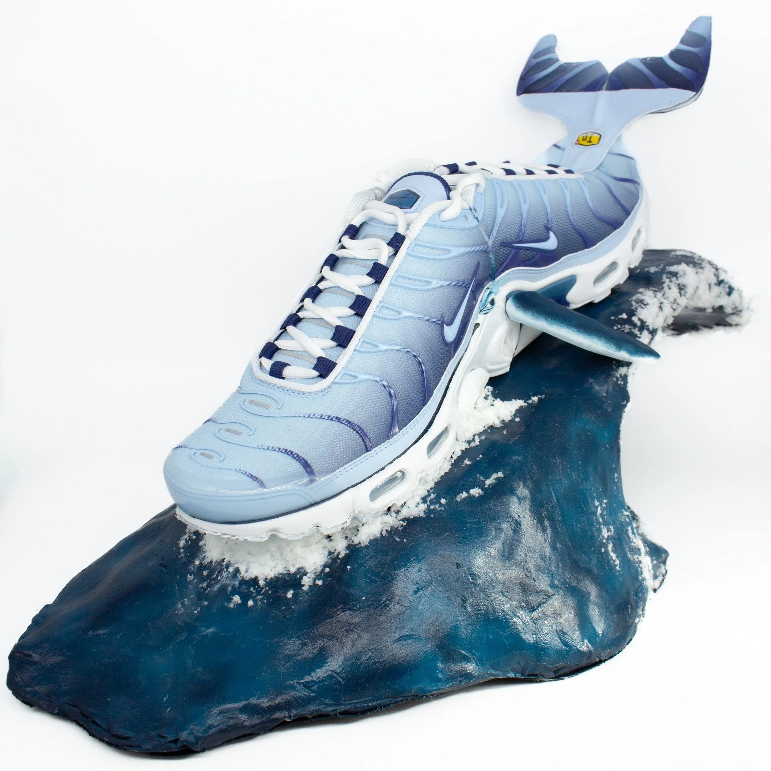 Sculpture of a Nike TN shoe resembling a whale, featuring a tail and fin, on a wave platform. Created in collaboration with Foot Locker.