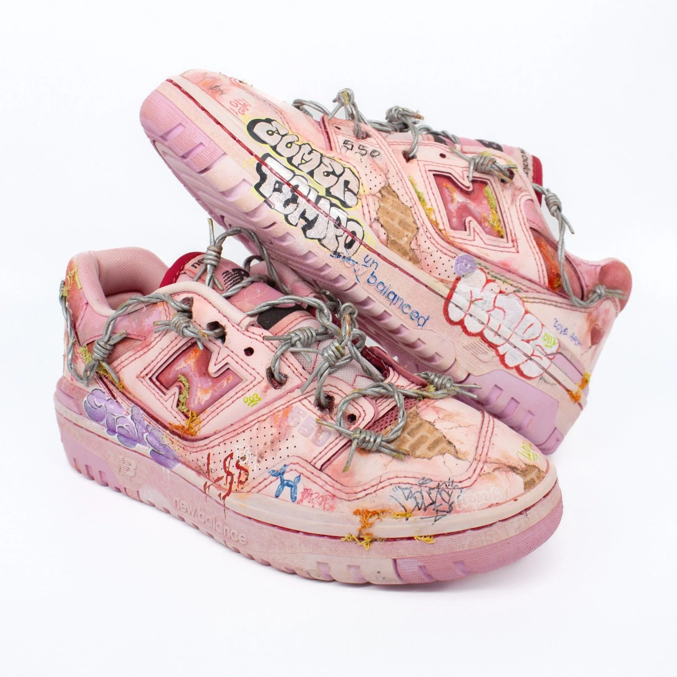 Pink New Balance sneakers with graffiti-style artwork and gray laces on a white background.