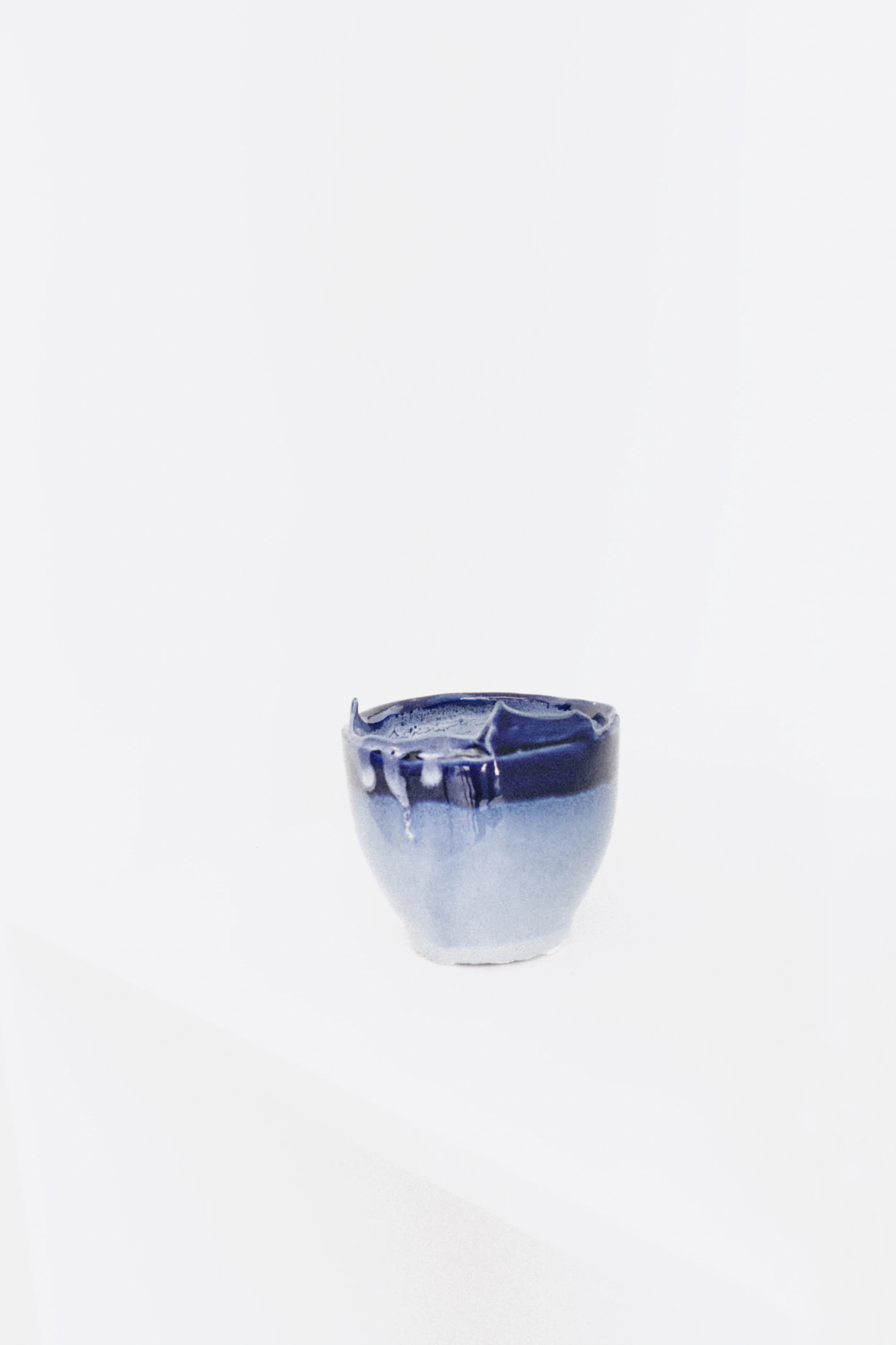 Blue handmade ceramic cup displayed in a minimalist white studio setting