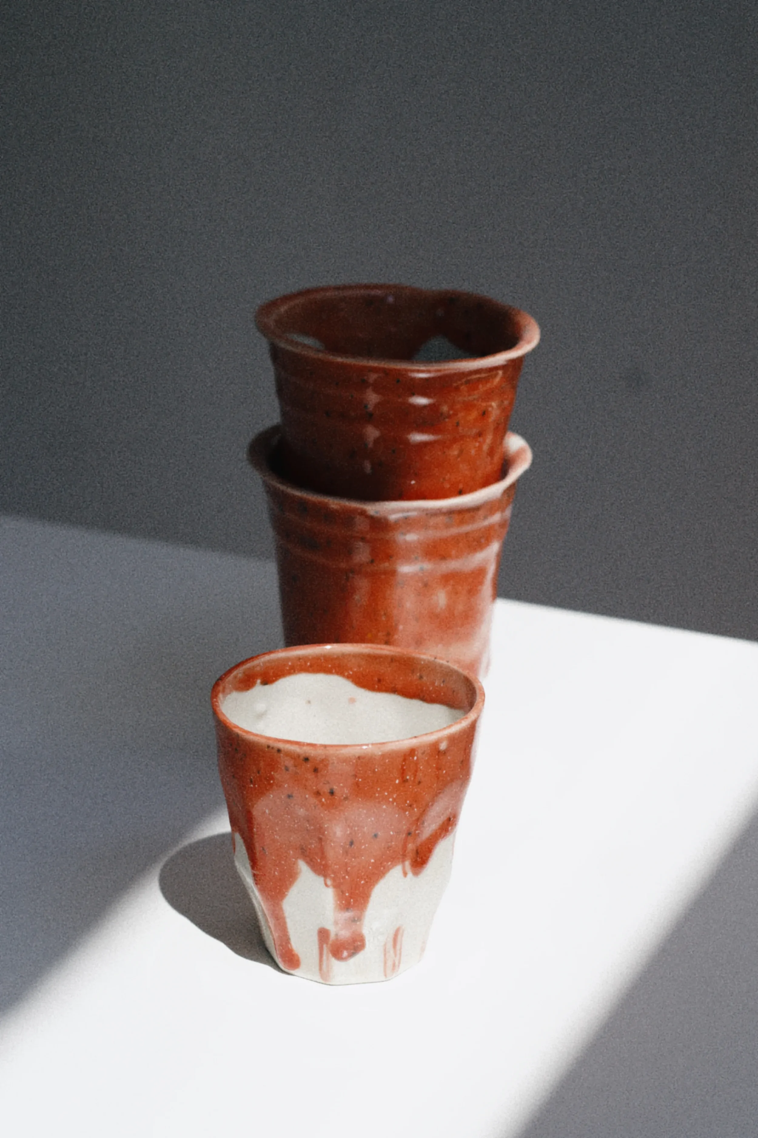 Stack of handmade red ceramic cups displayed in natural light for Marti Ceramic Studio