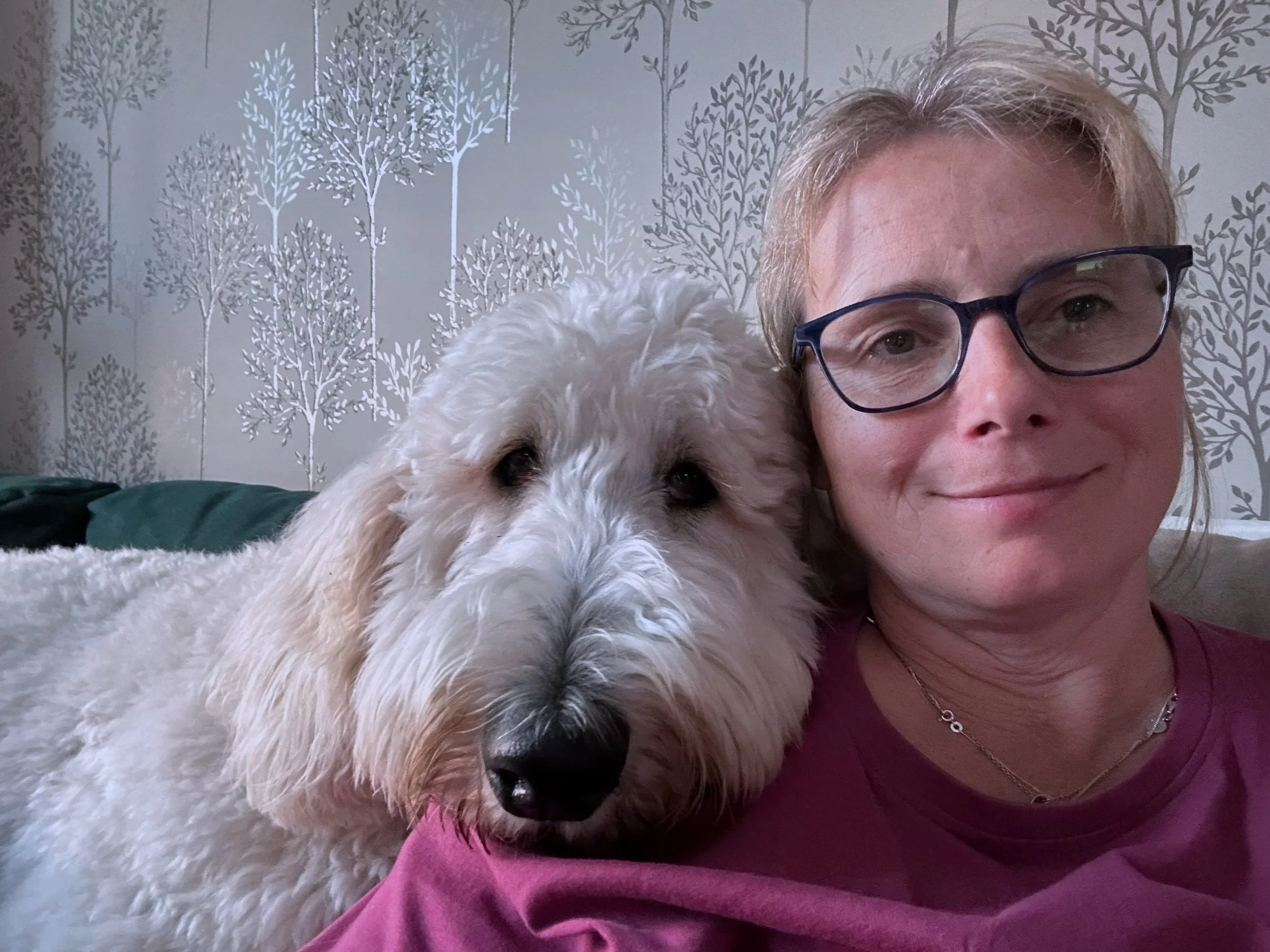 Beacon Mindset founder Justina Gilbert taking a selfie with Finn - Chief Companion Officer. The background features a wall with tree-patterned wallpaper.