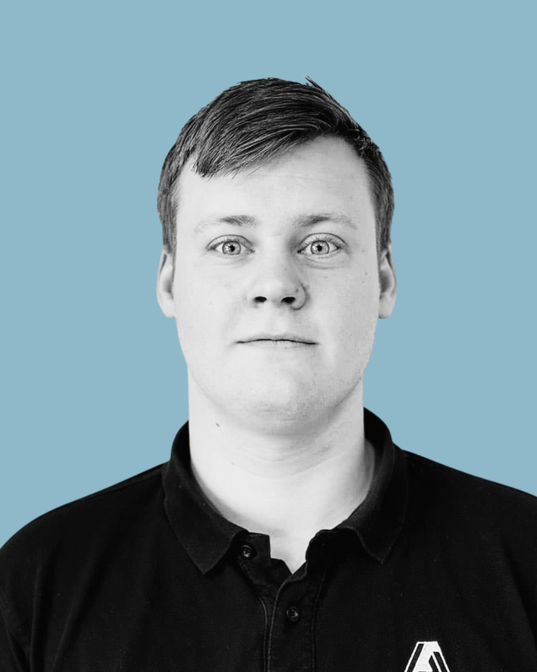 Svart-hvitt portrait av en ung mann med kort, mørkt hår, iført svart skjorte med krage, foran en lyseblå bakgrunn.