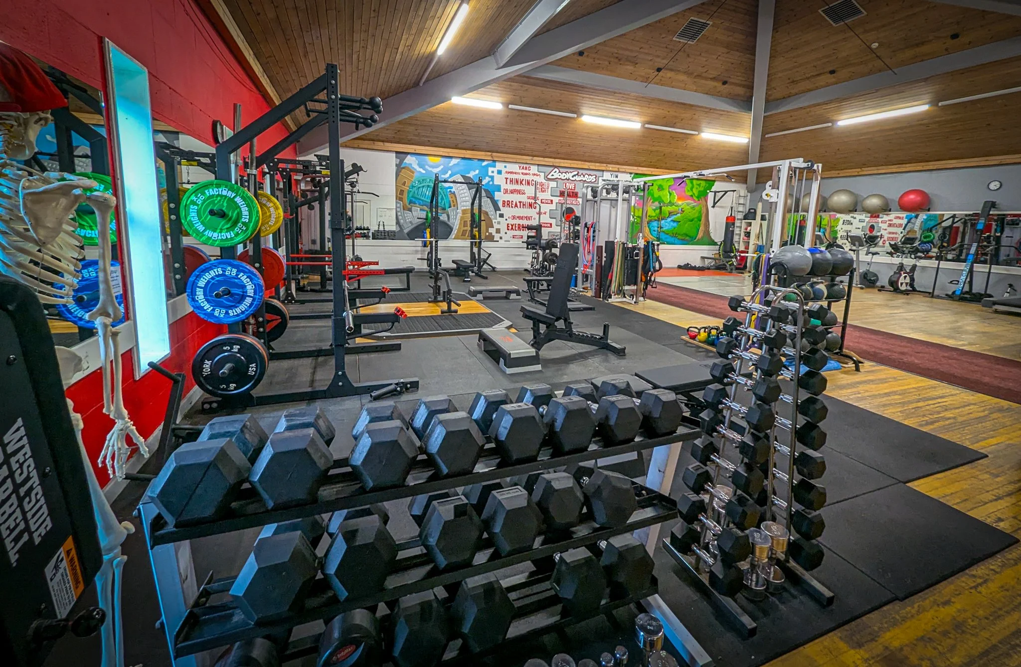 Indoor gym with weights, exercise equipment, and motivational murals on the wall.