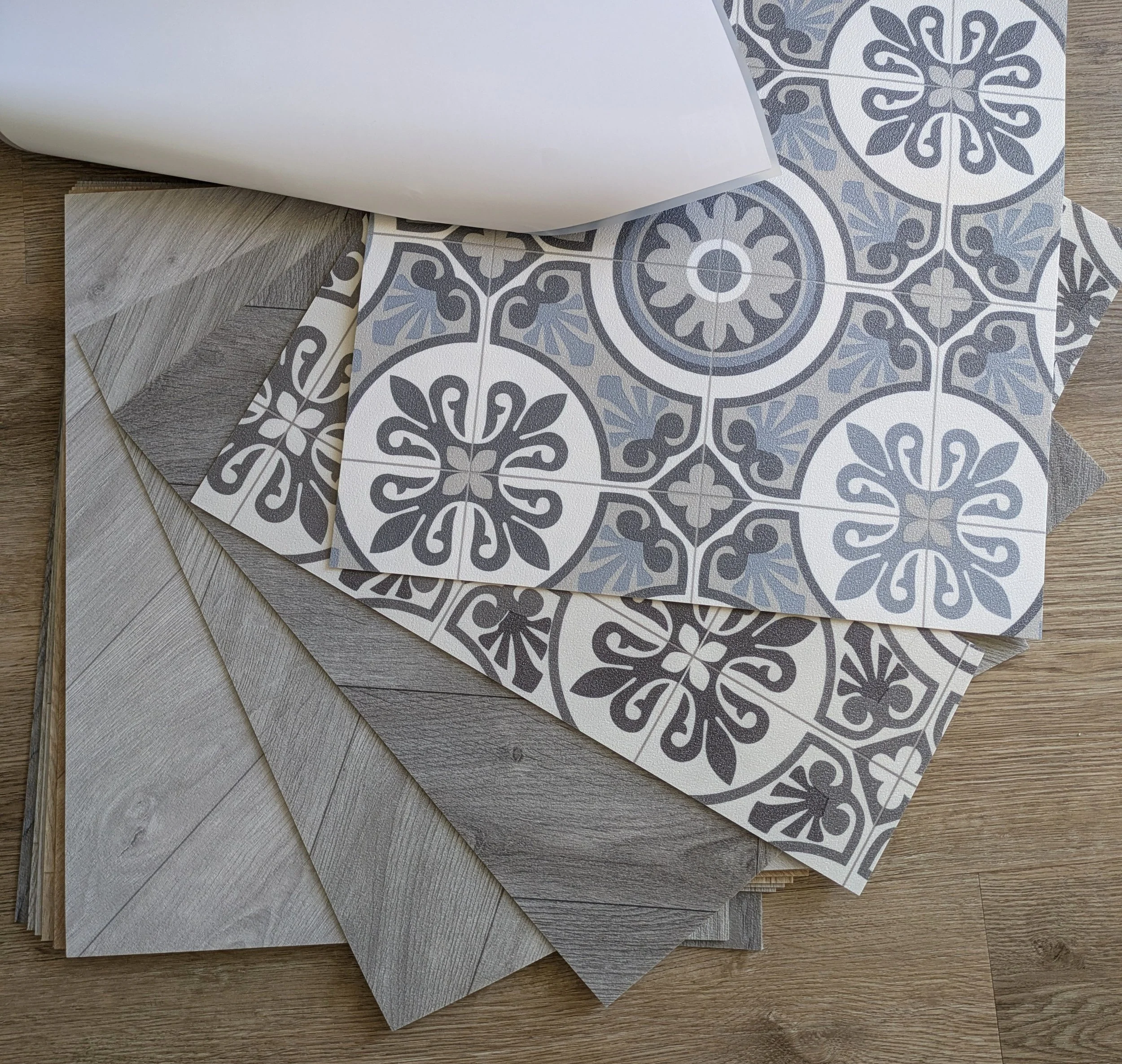Various patterned vinyl tiles and wood-look flooring sample swatches arranged on a wooden surface.