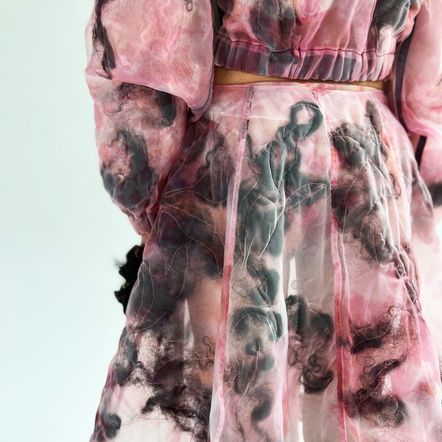 Close-up of a semi-transparent pink and black tie-dye hoodie and matching pants with a swirling pattern.