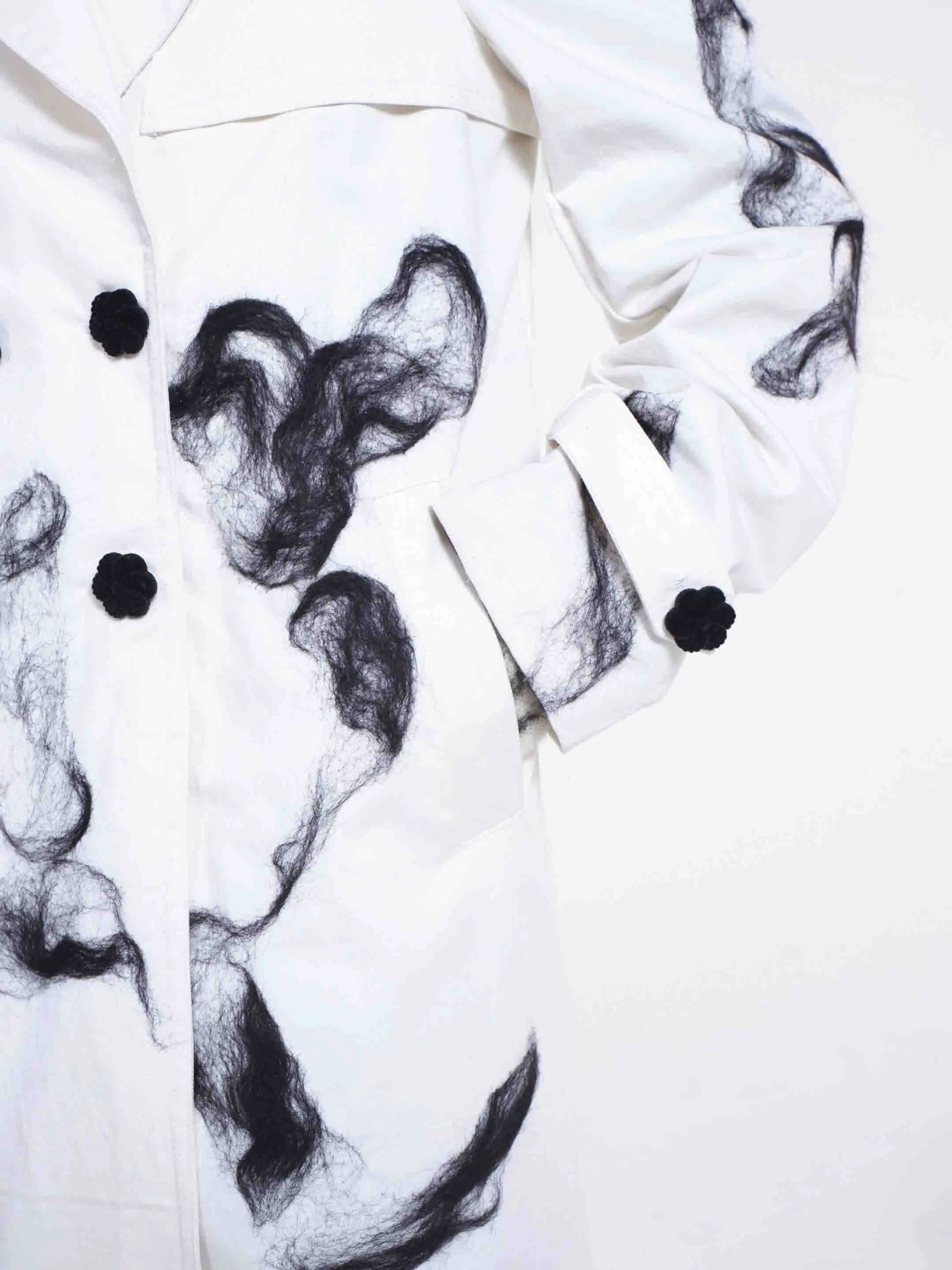 Detail of velvet flower-shaped buttons and hand-applied black wool on the Clara Pinto Mudlark Trench Coat
