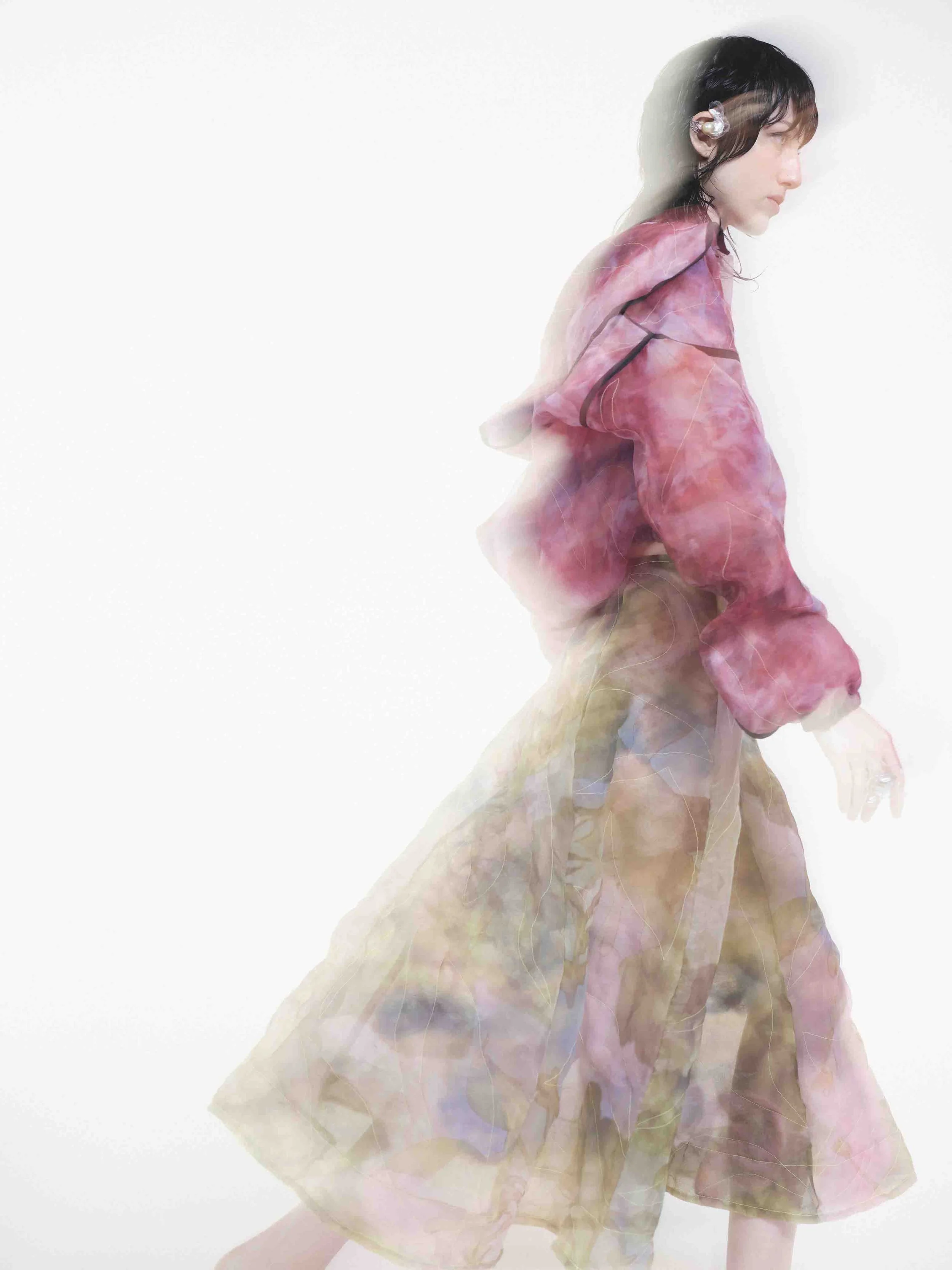 Person wearing a colorful, sheer outfit with blurred motion effect against a white background.