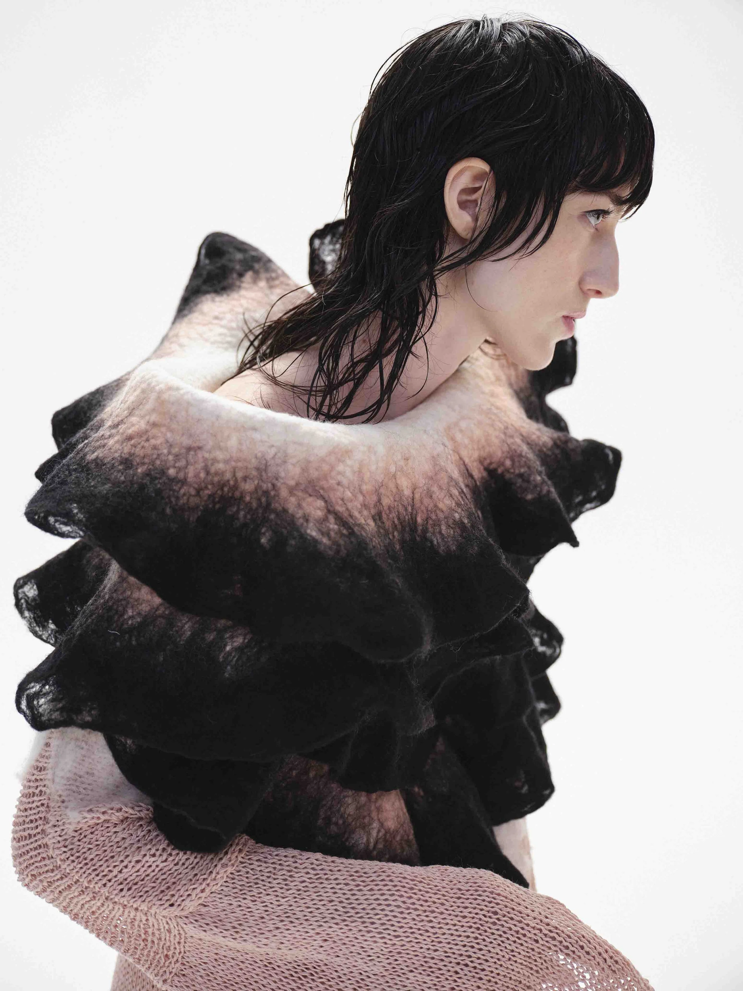 Person with dark hair wearing a ruffled, textured garment.