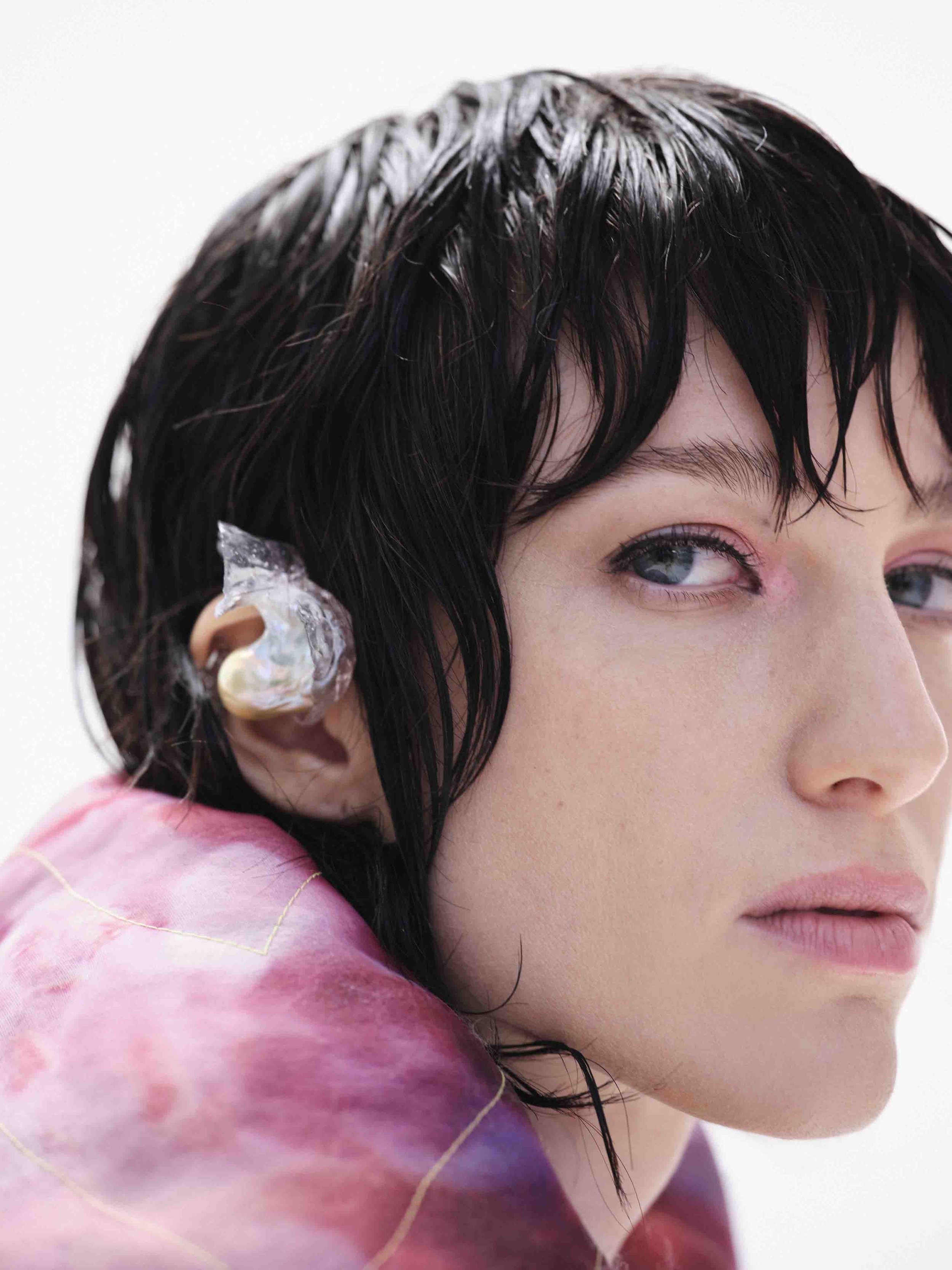 Close-up of a person with short, wet hair and an earpiece, wearing a pink and purple garment.
