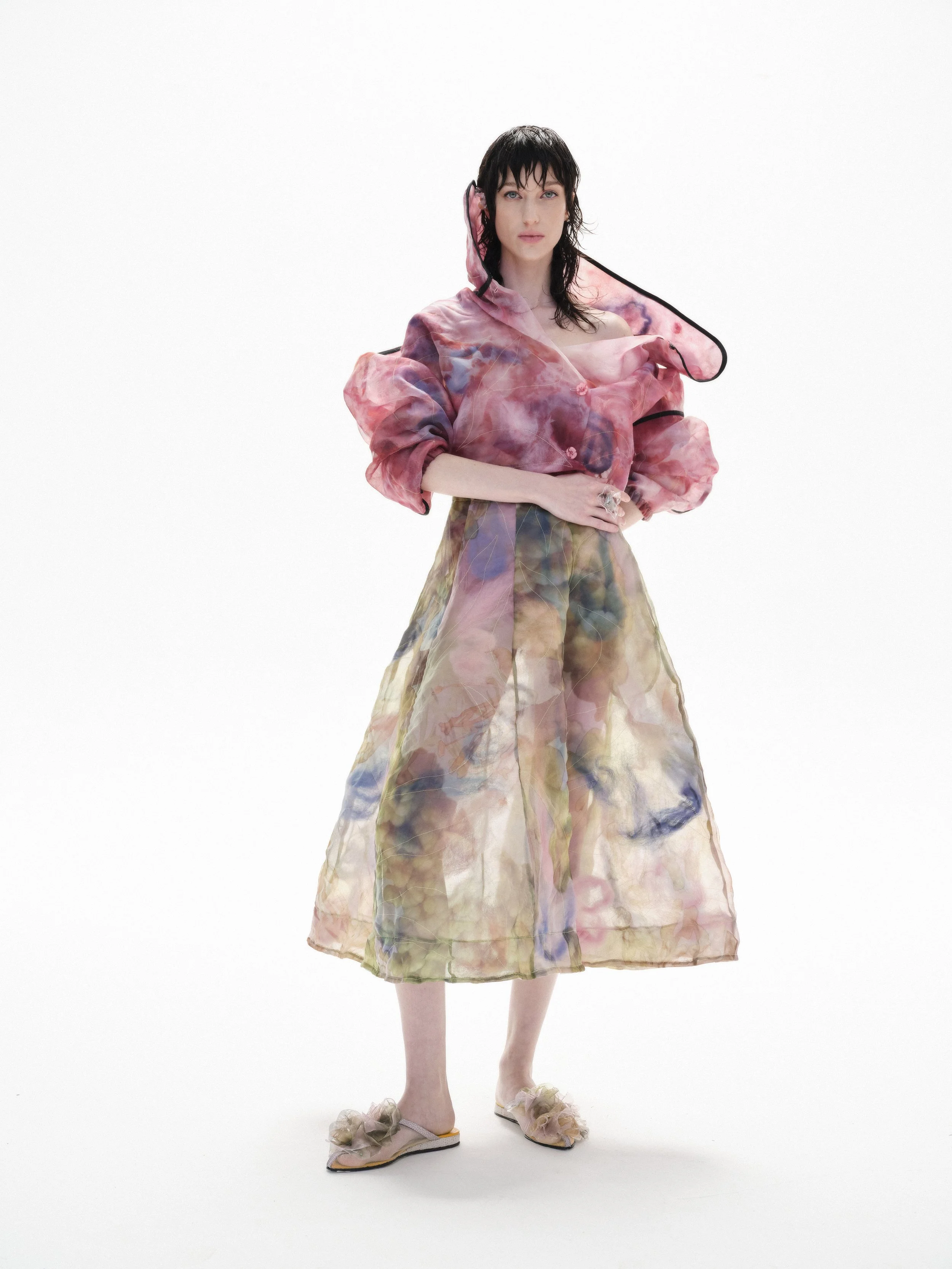 Person wearing a colorful, sheer outfit with floral patterns, standing against a white background.