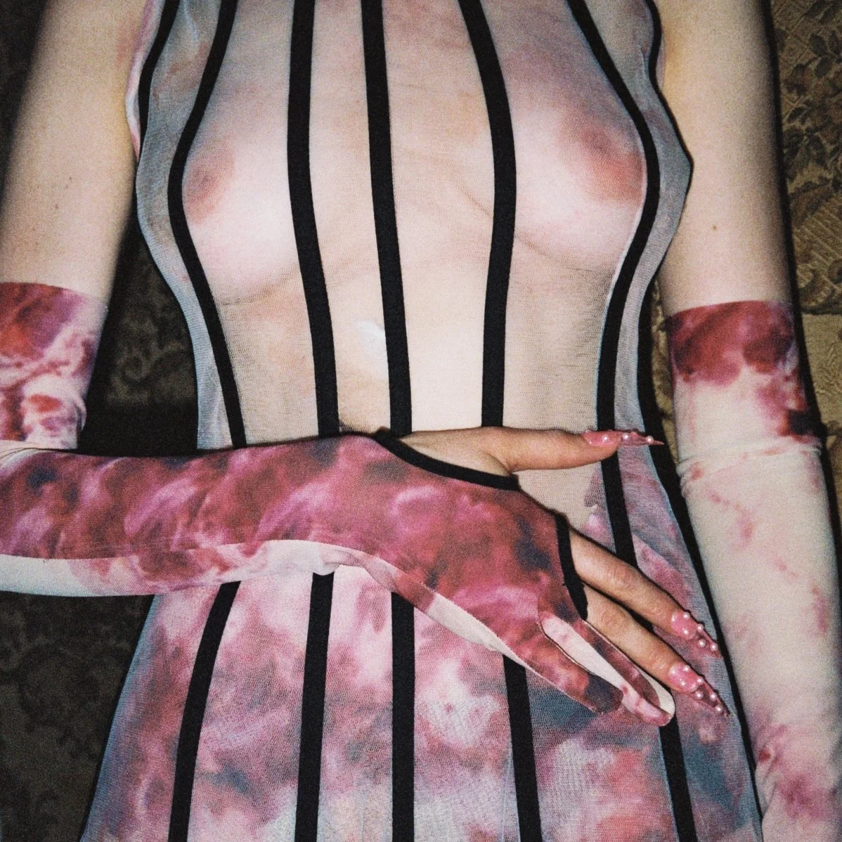 Person wearing a see-through striped dress with pink tie-dye gloves.