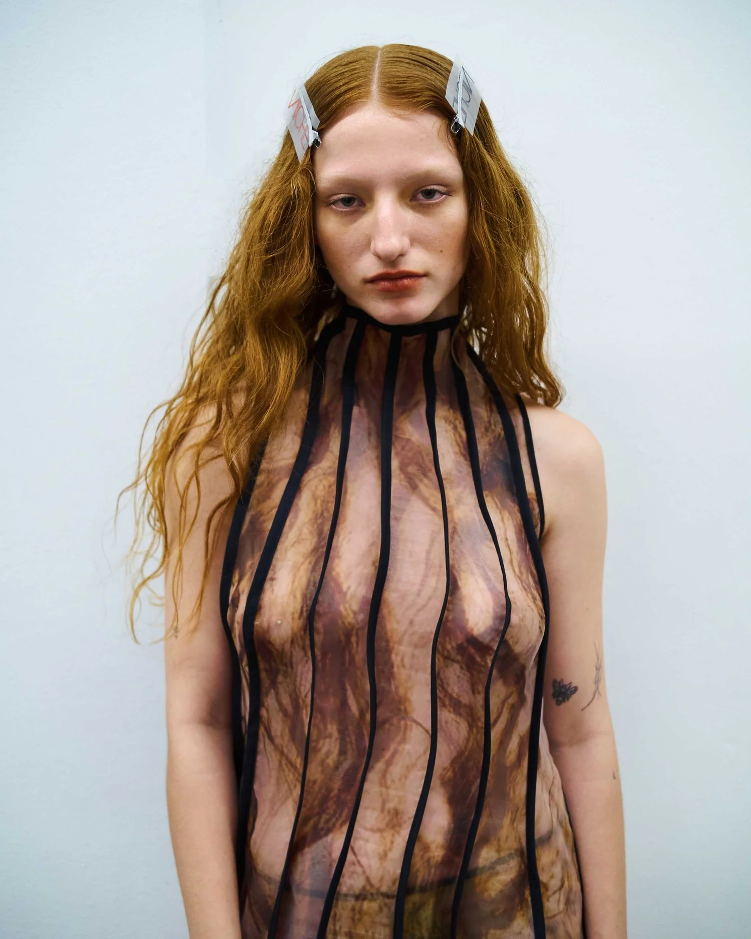 Person with long red hair wearing a sheer, patterned top and hair clips.