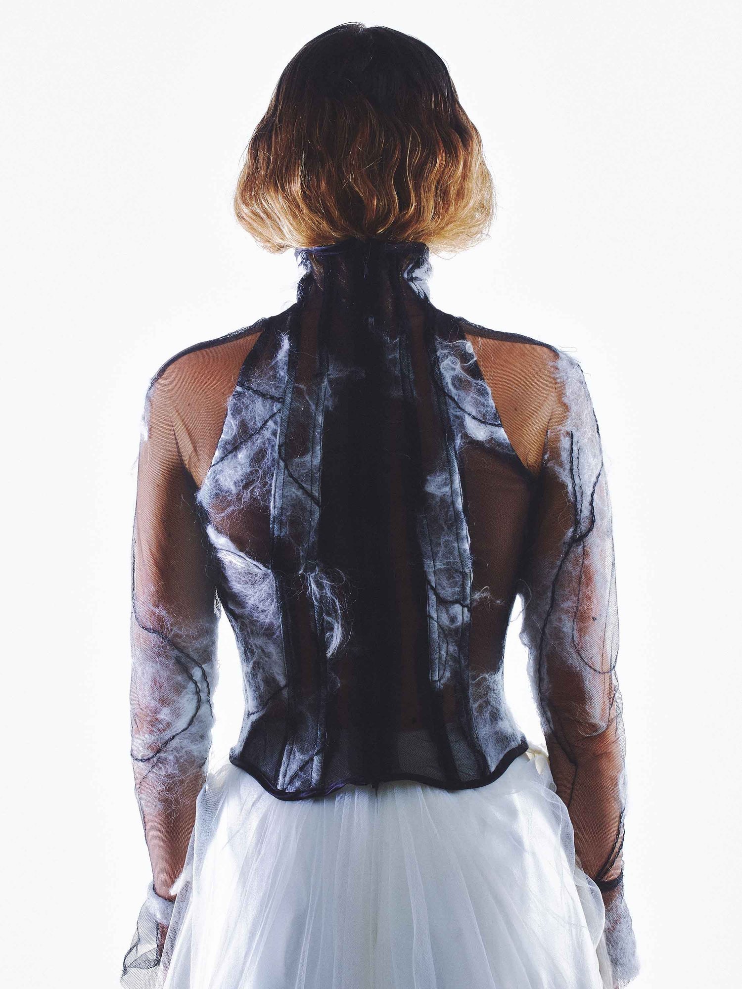 Person wearing a sheer black and white top with a white skirt, viewed from behind.