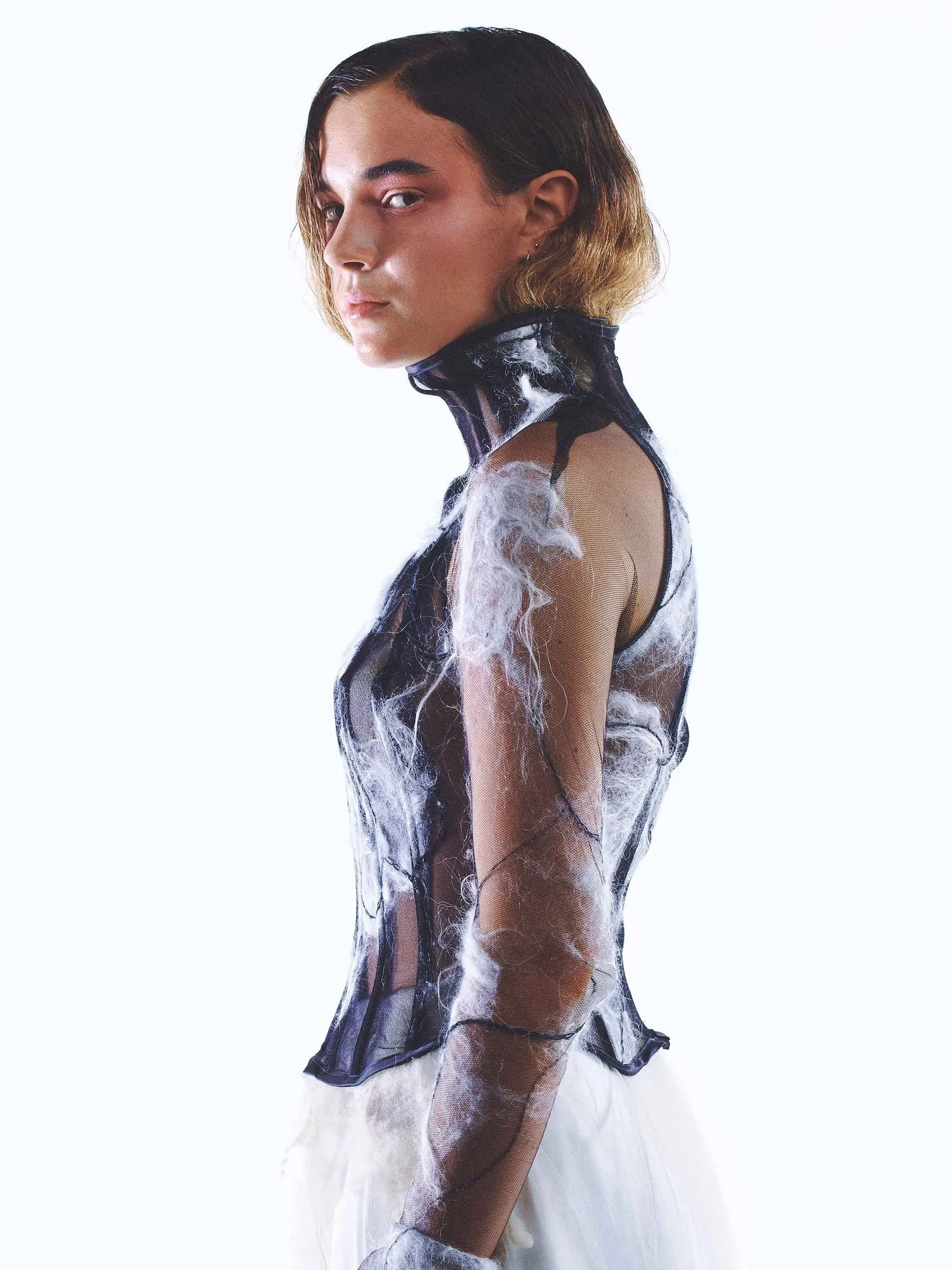 Person wearing a sheer black and white fashion garment, posing with a neutral expression.