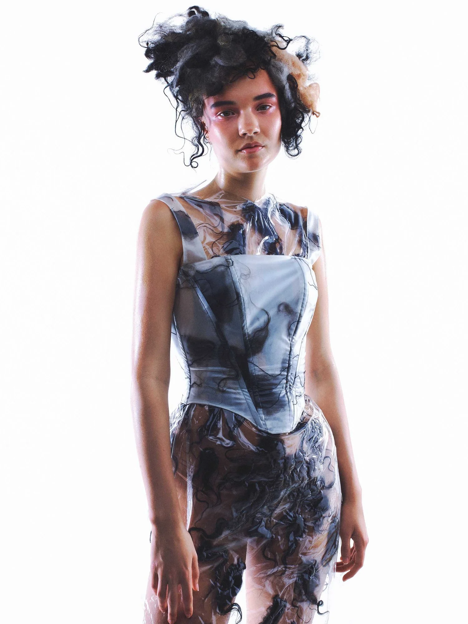 Person wearing a creative and artistic outfit with a sheer fabric overlay and a voluminous hairdo.