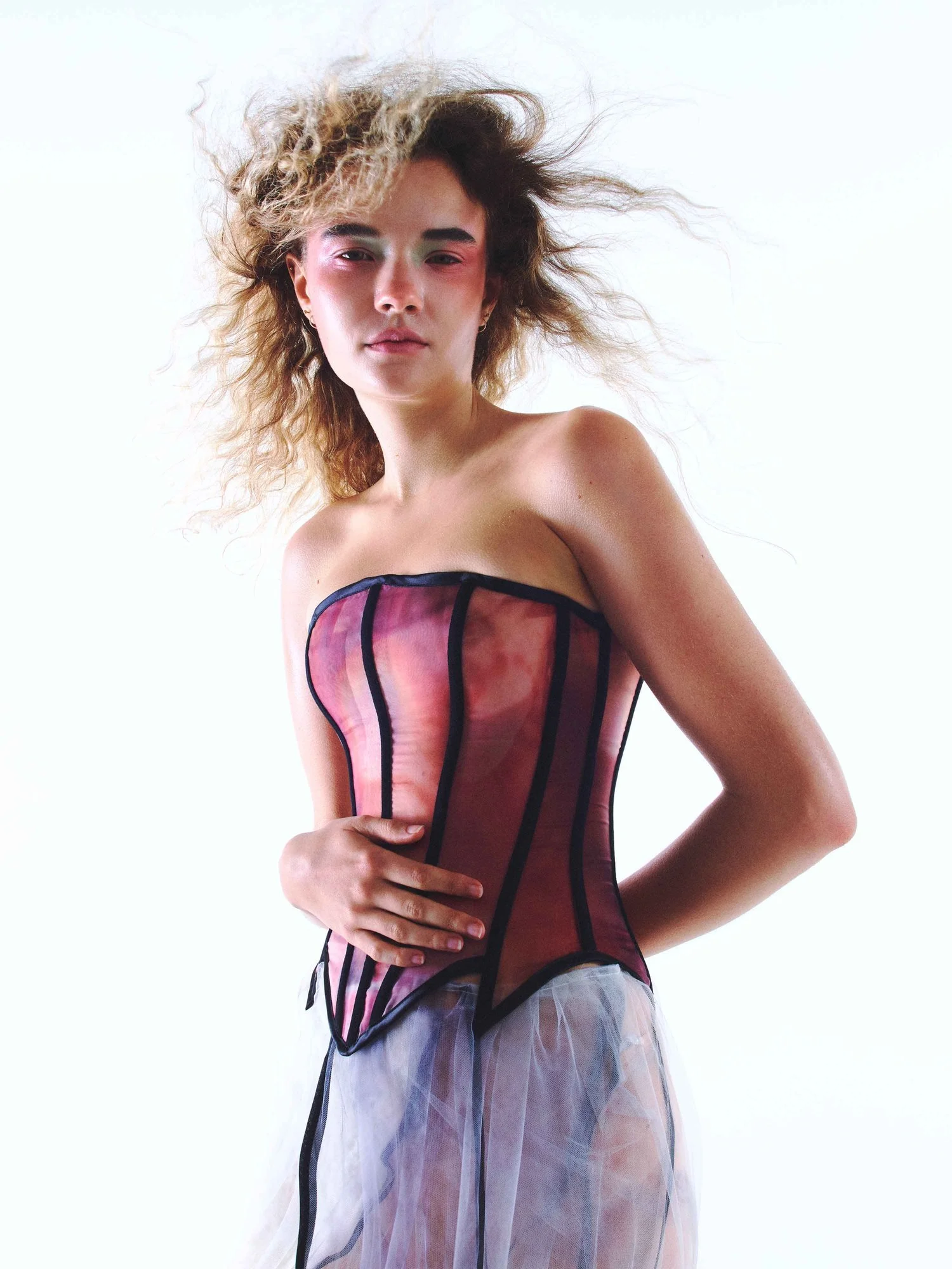 Person wearing a strapless corset with tulle skirt and wavy hair, posing against a white background.
