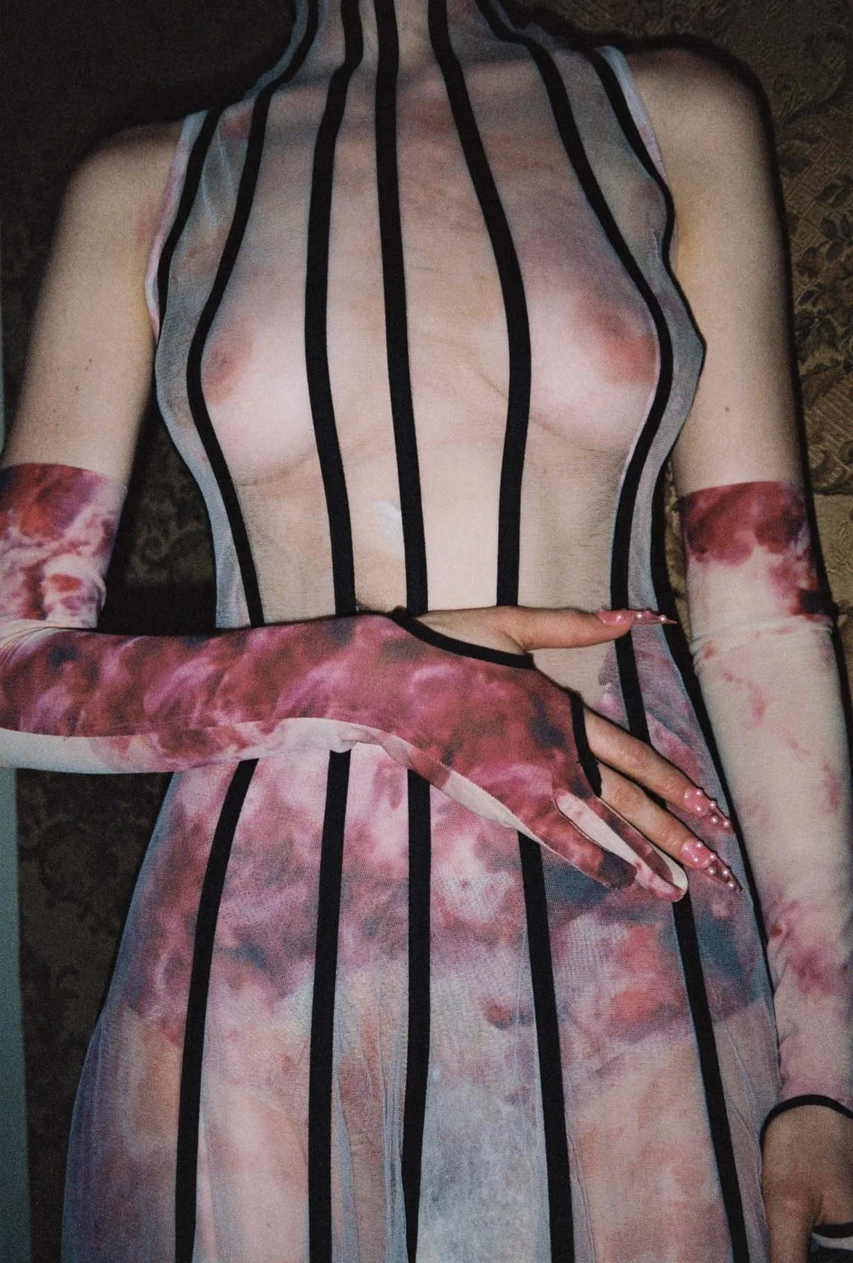 Person in transparent fashion outfit with vertical black lines and pink tie-dye pattern, wearing matching sleeves and long nails.