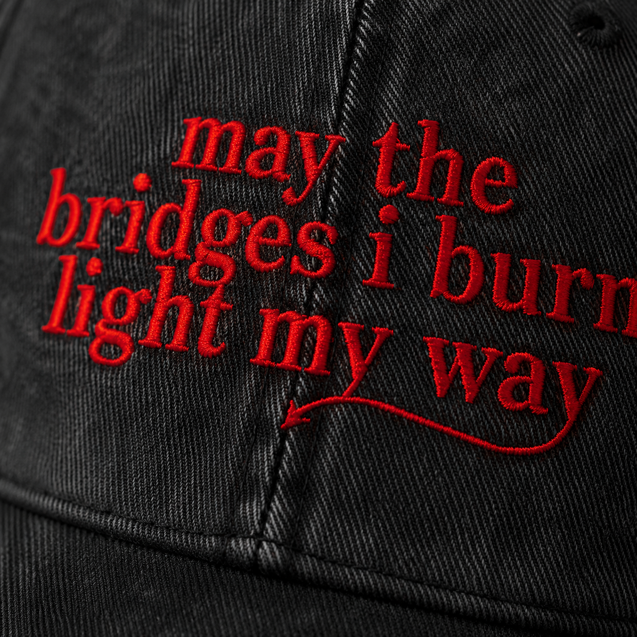 Close-up of black fabric with red embroidered text reading 'may the bridges I burn light my way'.