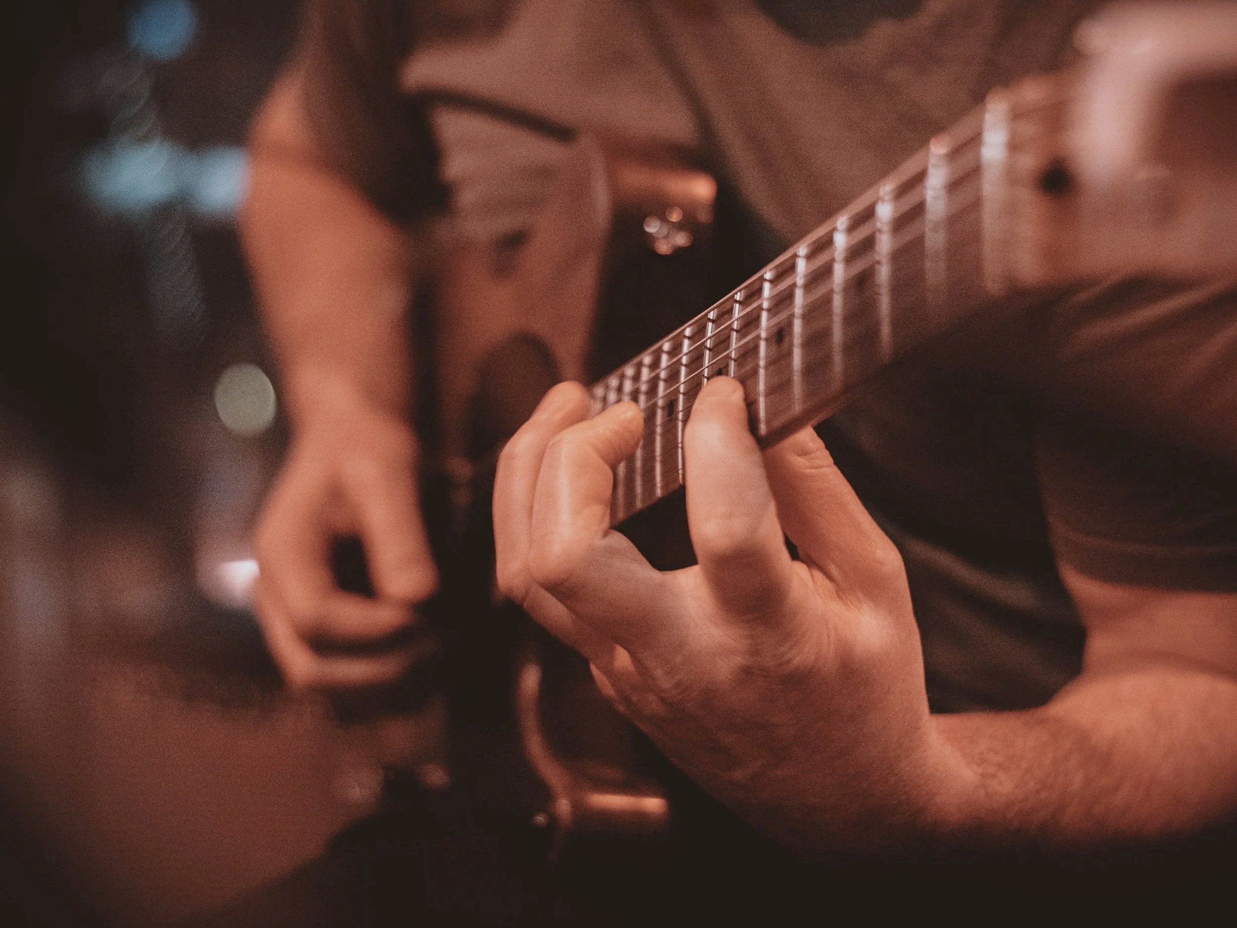 A person playing an acoustic guitar, focusing on their left hand on the fretboard.