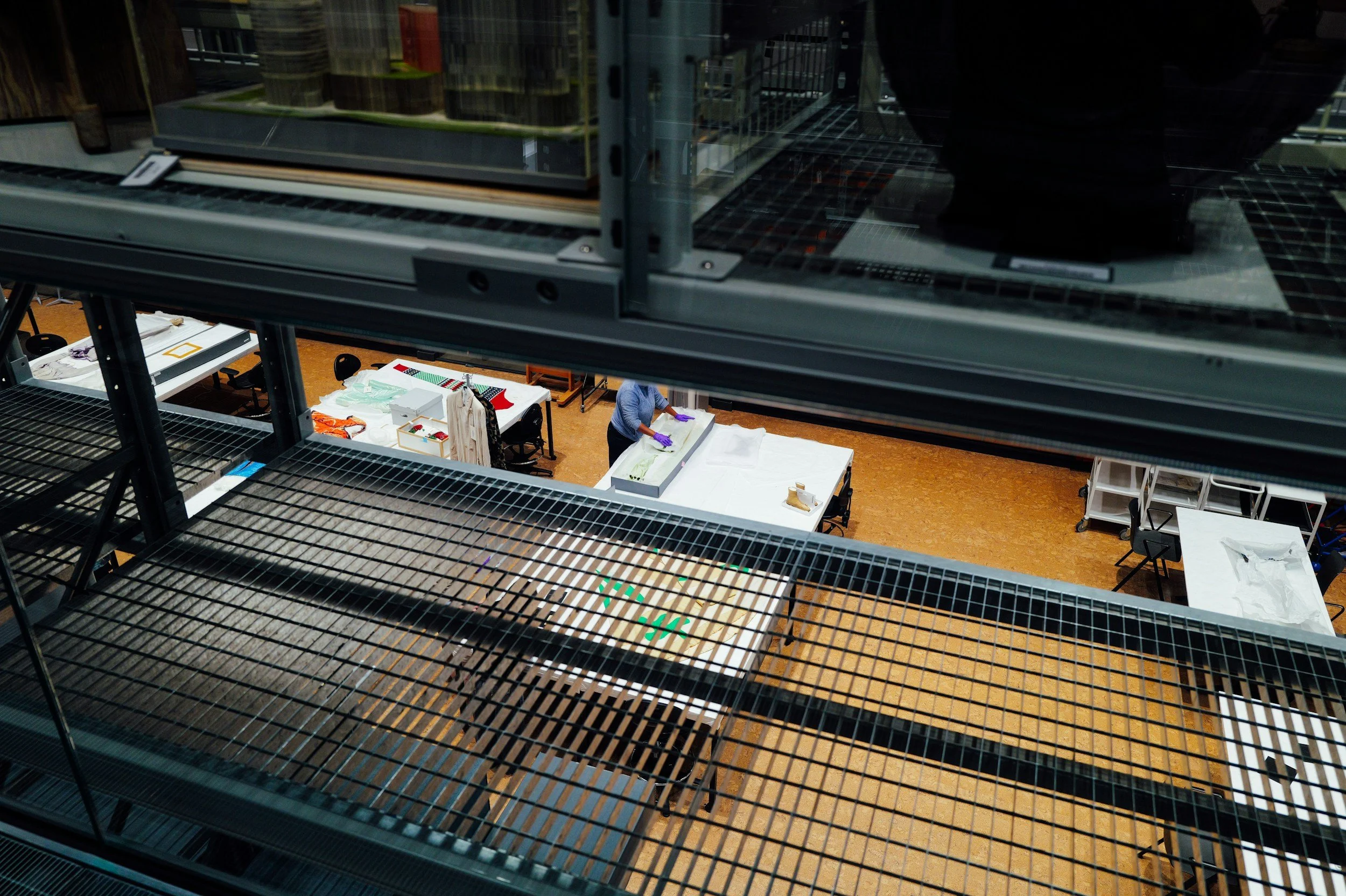 View of a storage rack in a warehouse or manufacturing facility, with a person working on a table below.